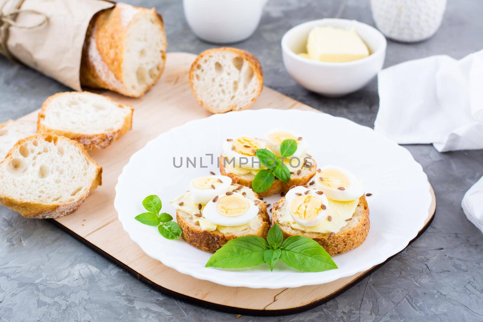 Hearty breakfast in the morning. Fresh baguette sandwiches with butter, quail eggs, flax seeds and basil seeds on a plate on the table by Aleruana