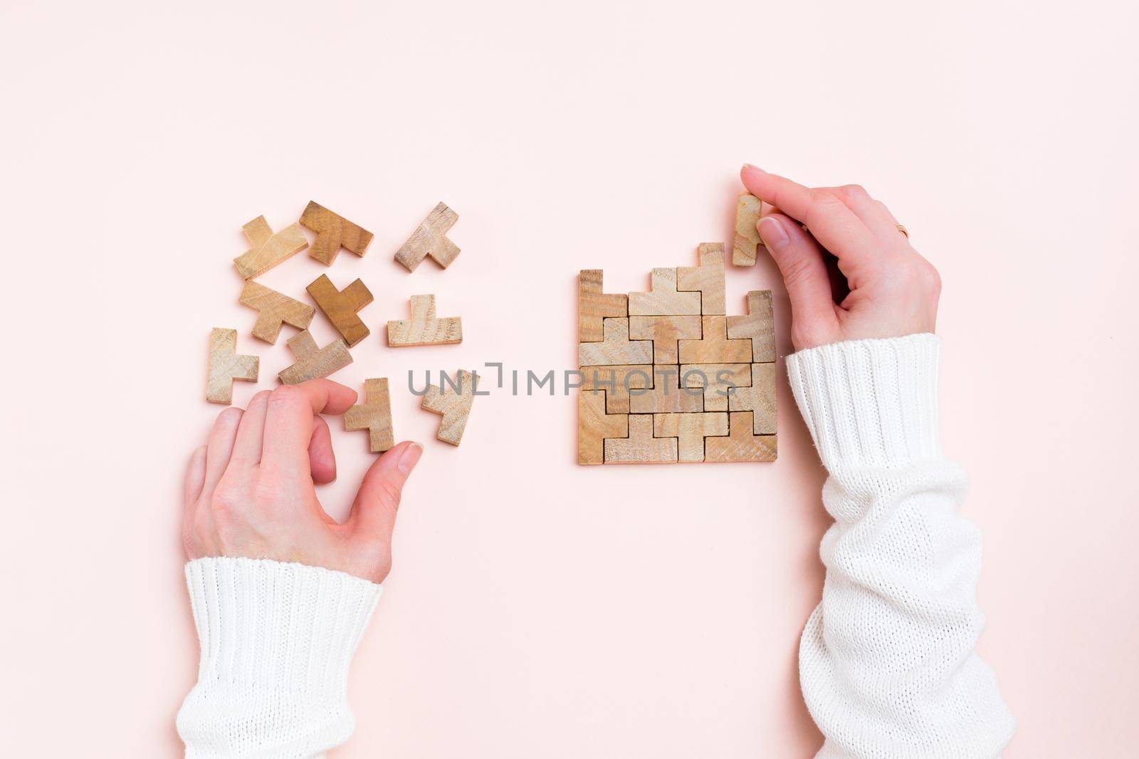 Organization and order. Female hands lay out wooden puzzle pieces on a pink background. Top view