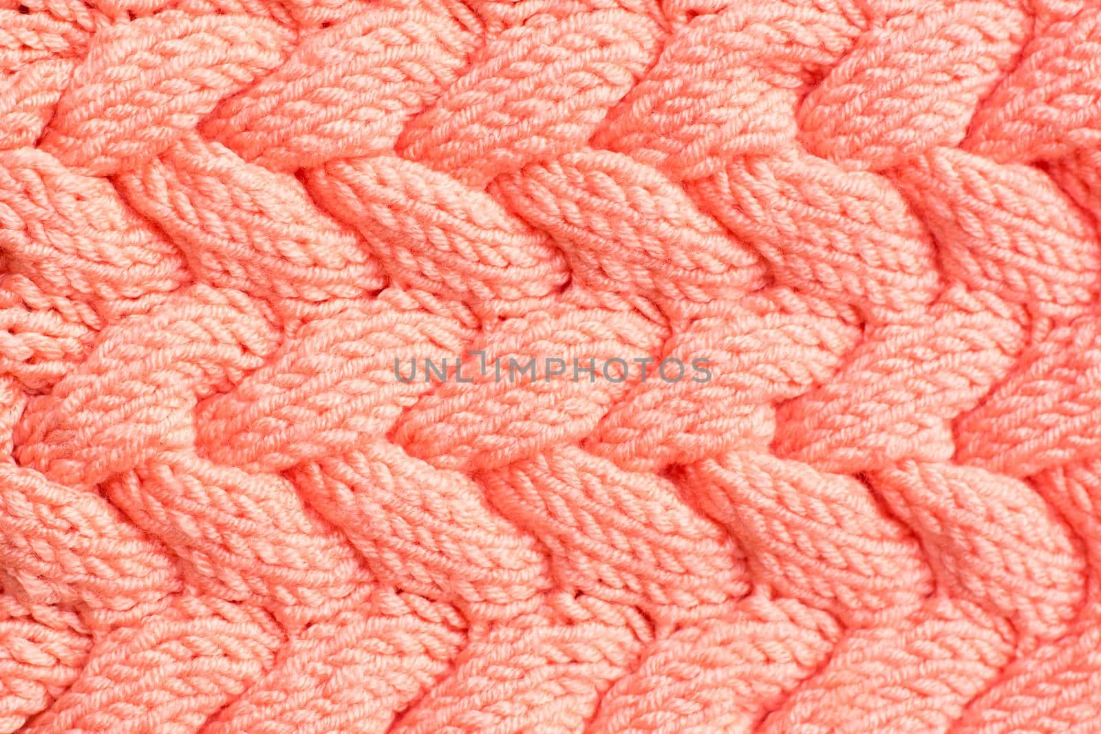 Textured background. Knitted fabric in peach color in the form of intertwined braids. Top view