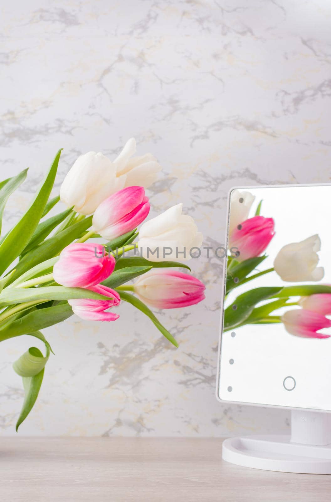 A bouquet of white and pink tulips with green leaves stands in a jug on the table and is reflected in the mirror. Selective focus. Vertical view