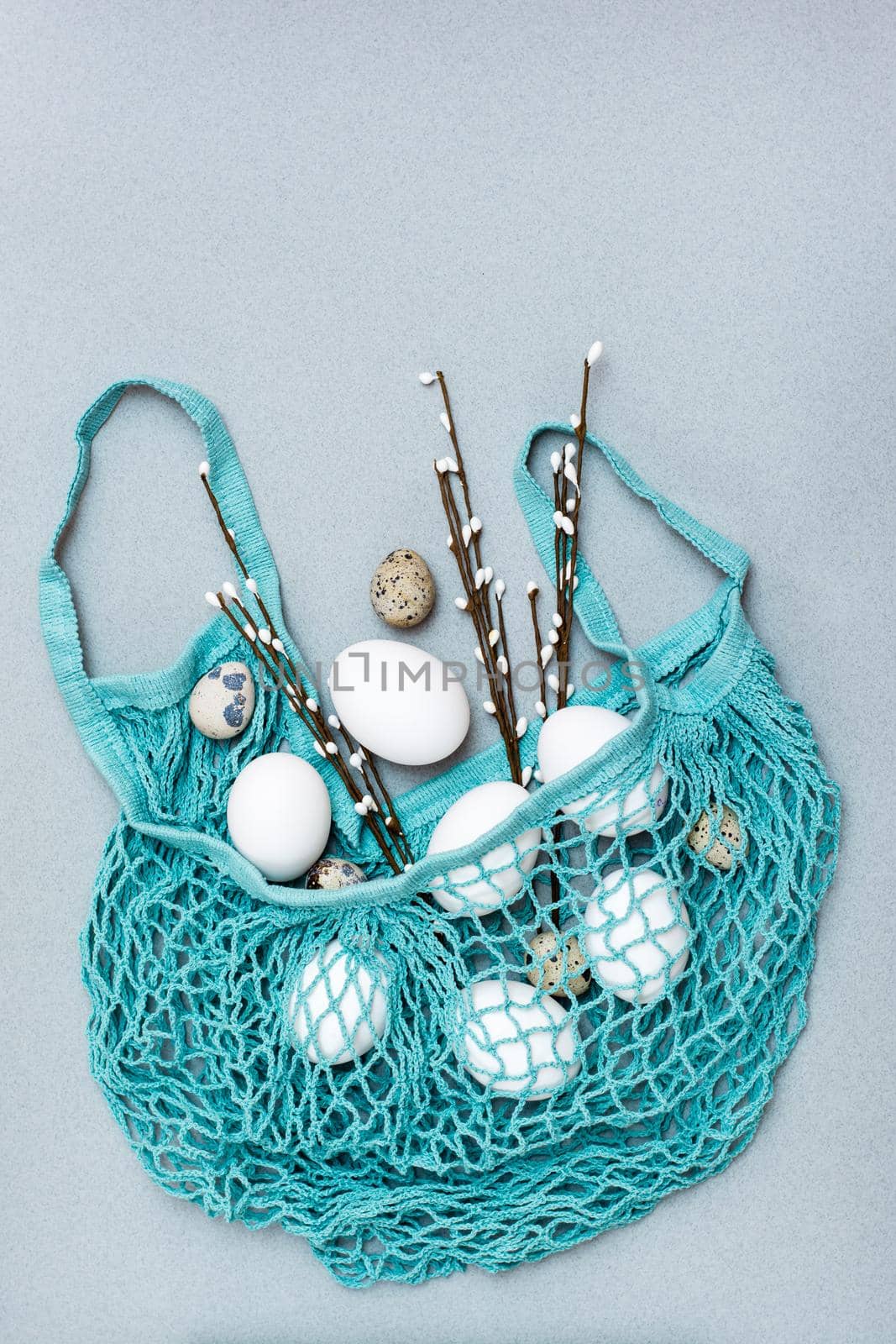 Happy Easter. Eggs and pussy willow branches in a mesh bag on a gray background. Top view