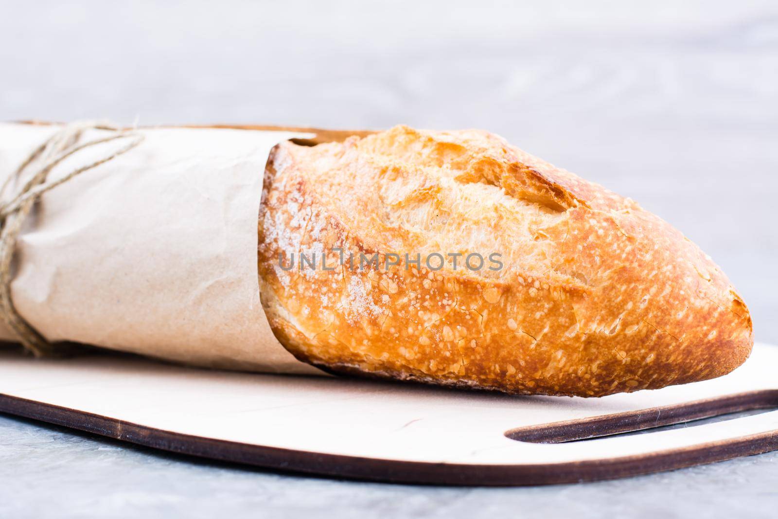 Fresh baguette in wrapping paper on cutting board on table. Close-up by Aleruana