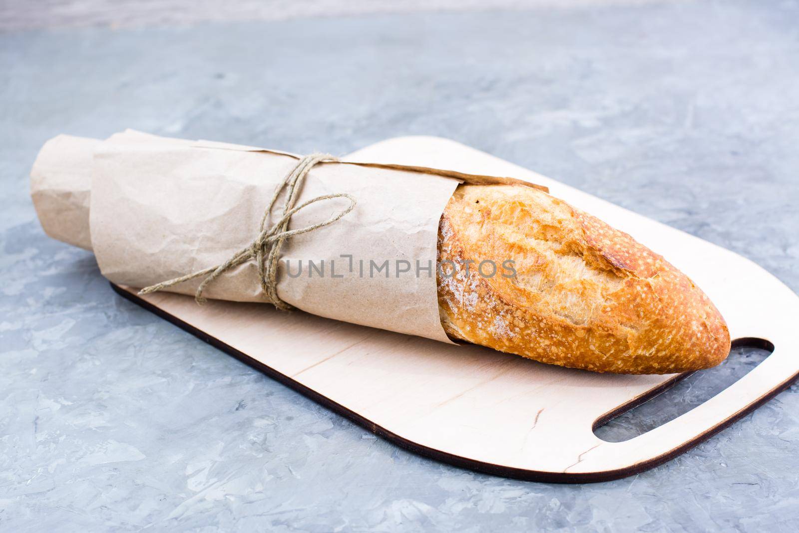 Fresh baguette in wrapping paper on cutting board on table