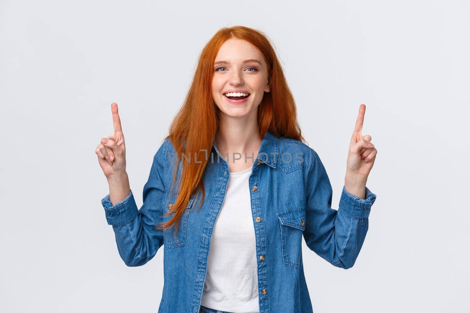 Cheerful outgoing alluring redhead woman, long red hairstyle, showing top promo, pointing fingers up and laughing, smiling amused, leave positive review, blogger visit awesome place, white background.