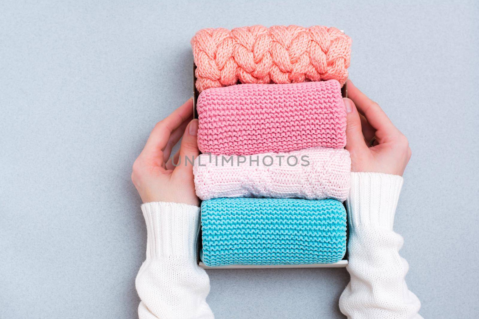 Organization and order. Women's hands hold a box of neatly folded knitted clothes. Top view
