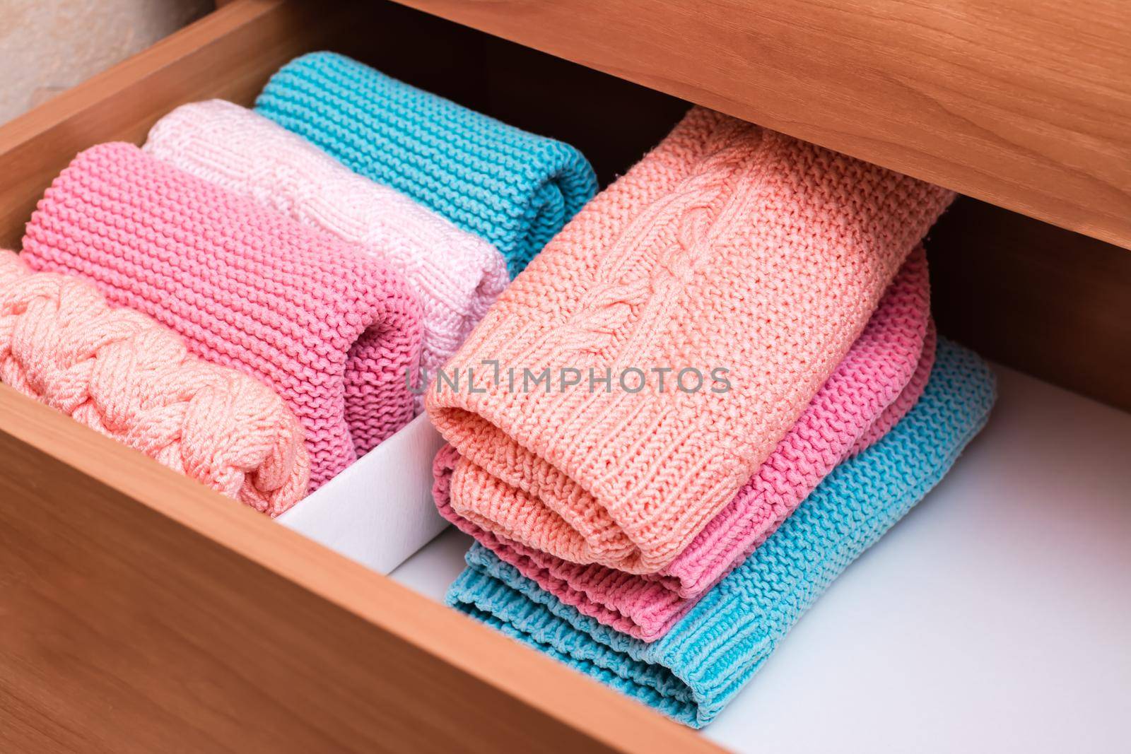 Organization and order. A stack of knitted clothes next to a box of neatly folded items in a dresser drawer by Aleruana