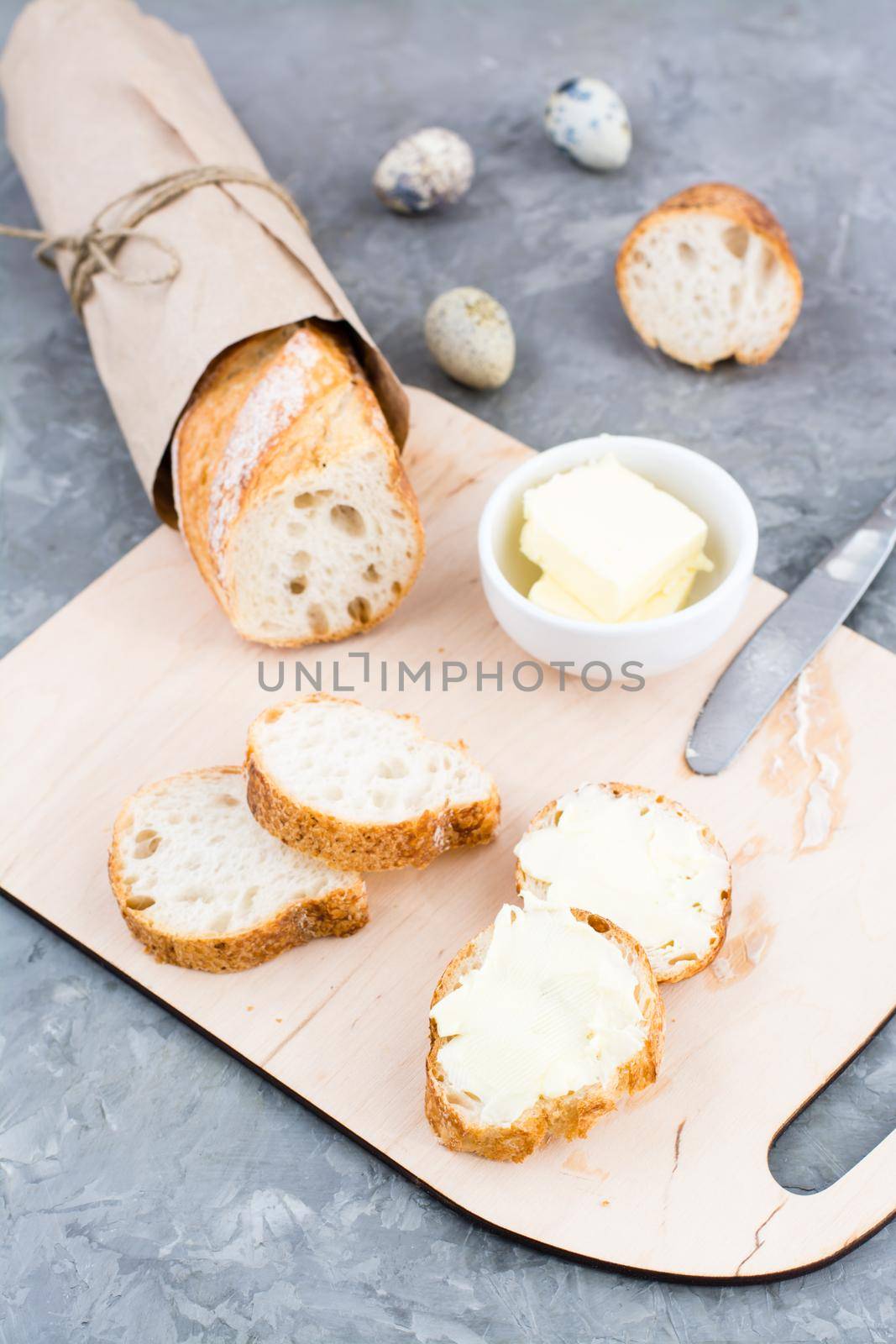 Tasty breakfast. Fresh baguette sandwiches with butter and quail eggs on a cutting board on the table. Vertical view