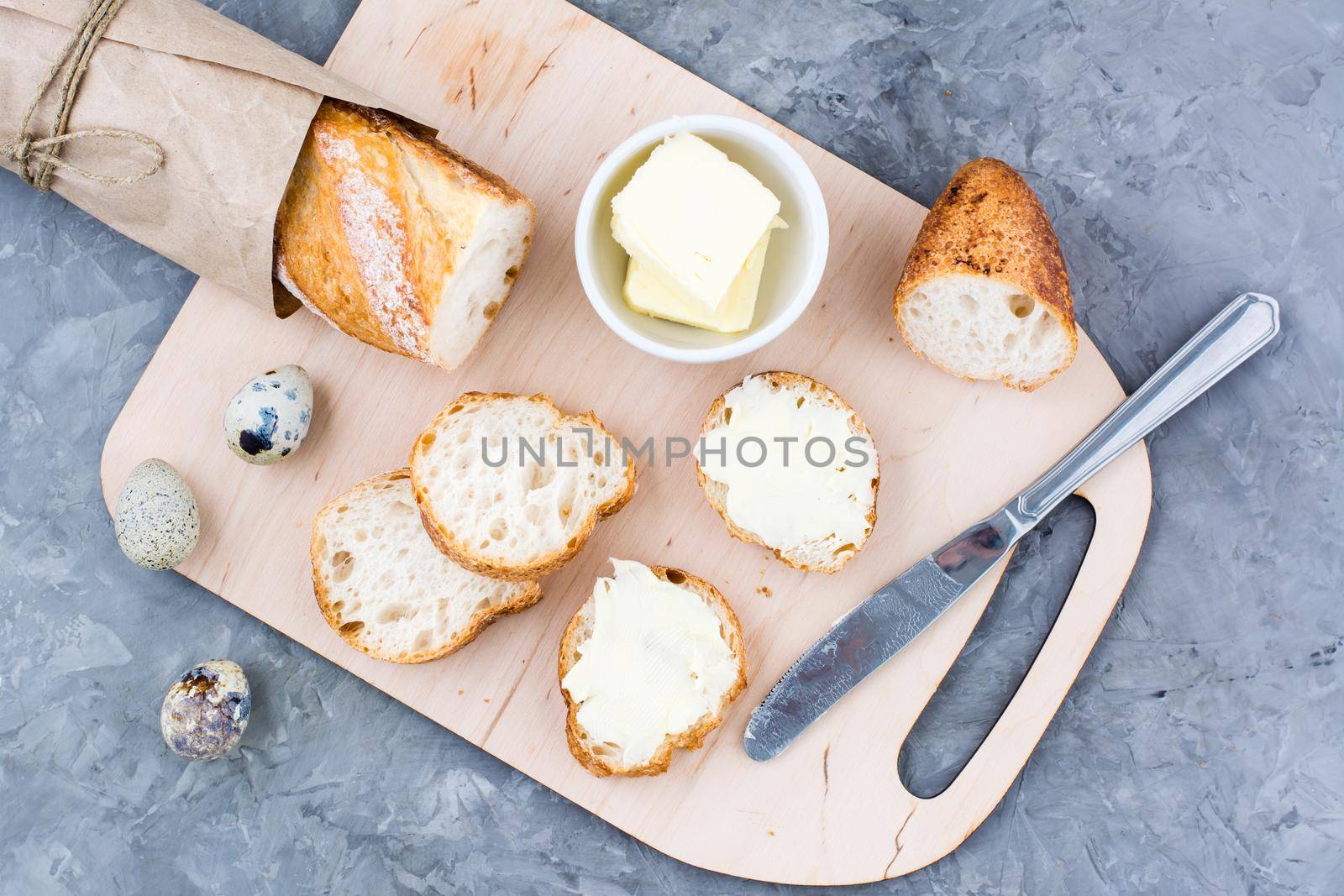 Tasty breakfast. Fresh baguette sandwiches with butter and quail eggs on a cutting board on the table. Top view