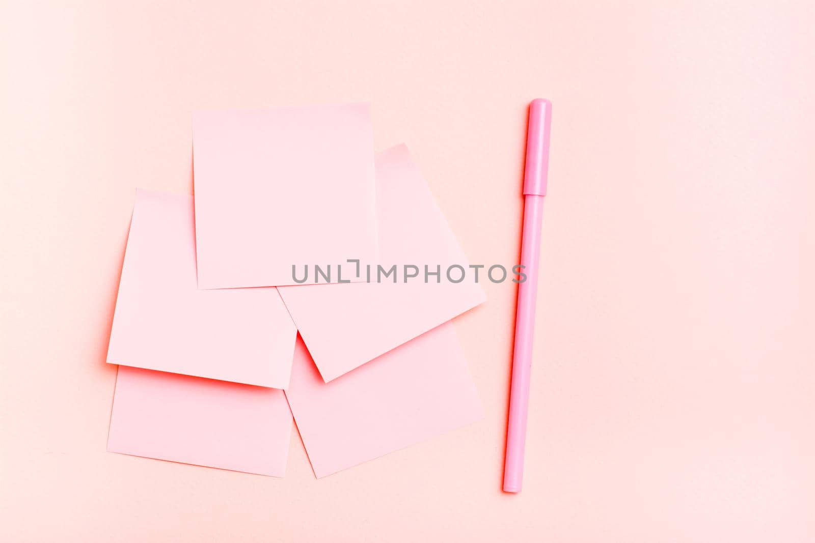 The concept is pink. Blank square small sheets of paper and a pen on a pink background. Top view