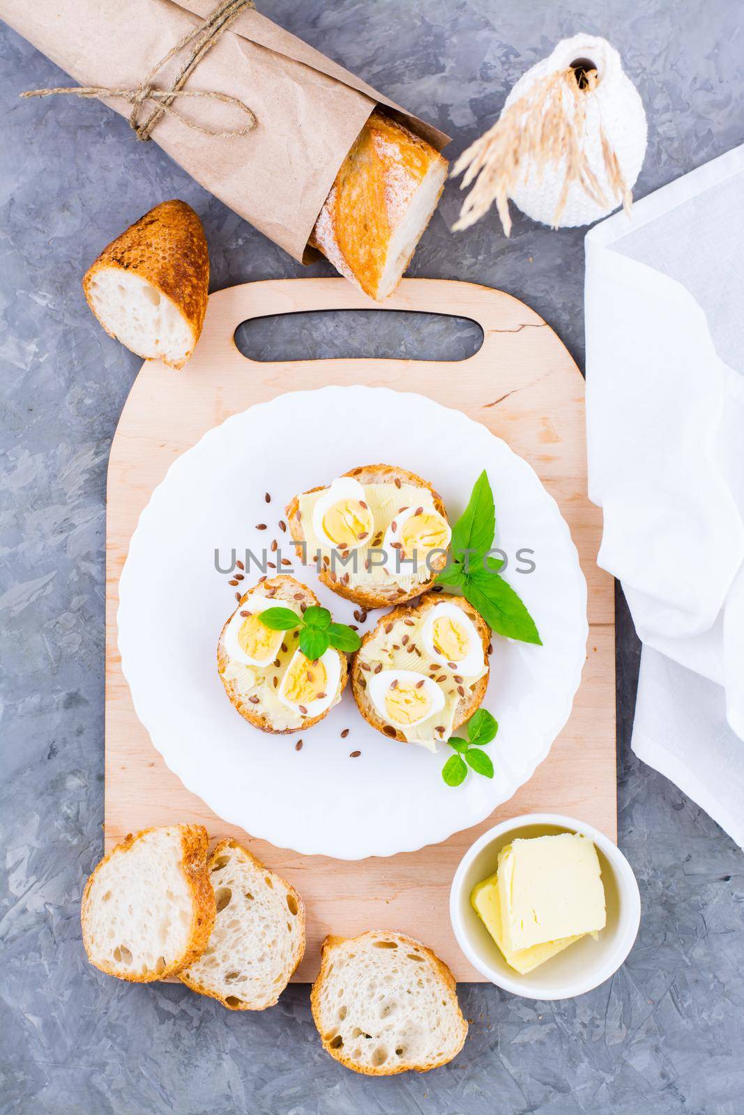 Hearty breakfast in the morning. Fresh baguette sandwiches with butter, quail eggs, flax seeds and basil seeds on a plate on the table. Top and vertical view