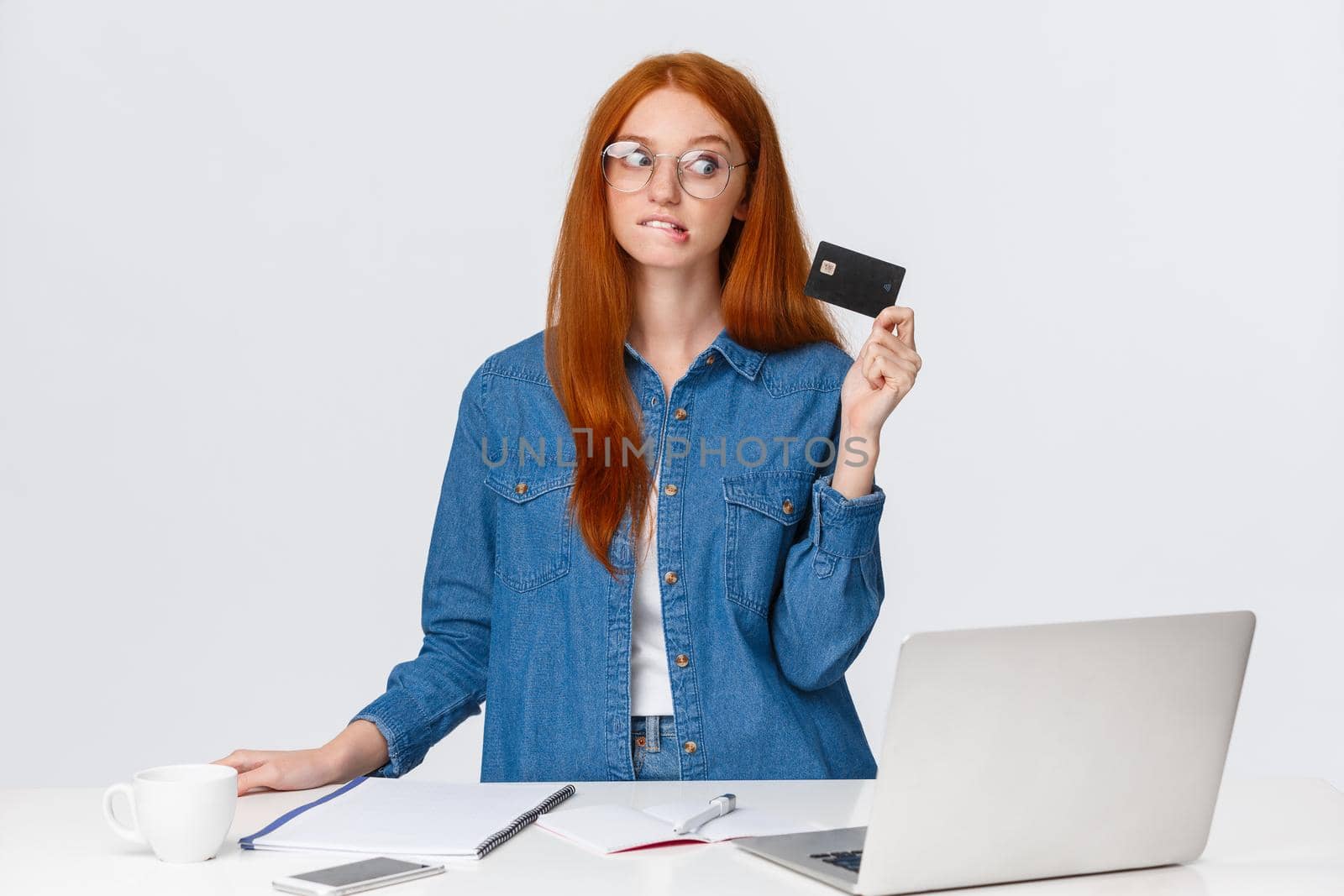 Shopaholic trying hold herself from buying new things during online discounts, biting lip eager waste some money, looking credit card tempting, shopping internet, white background.