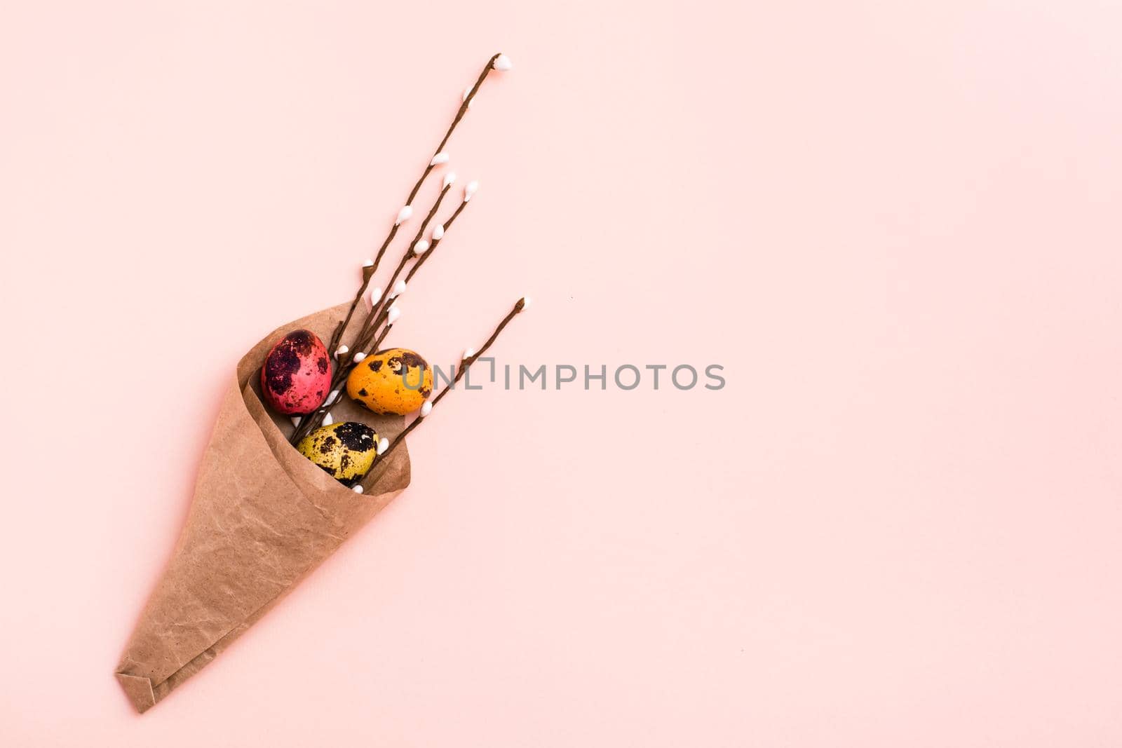 Happy Easter. Bouquet of painted quail eggs and pussy willow branches wrapped in brown paper on pink background