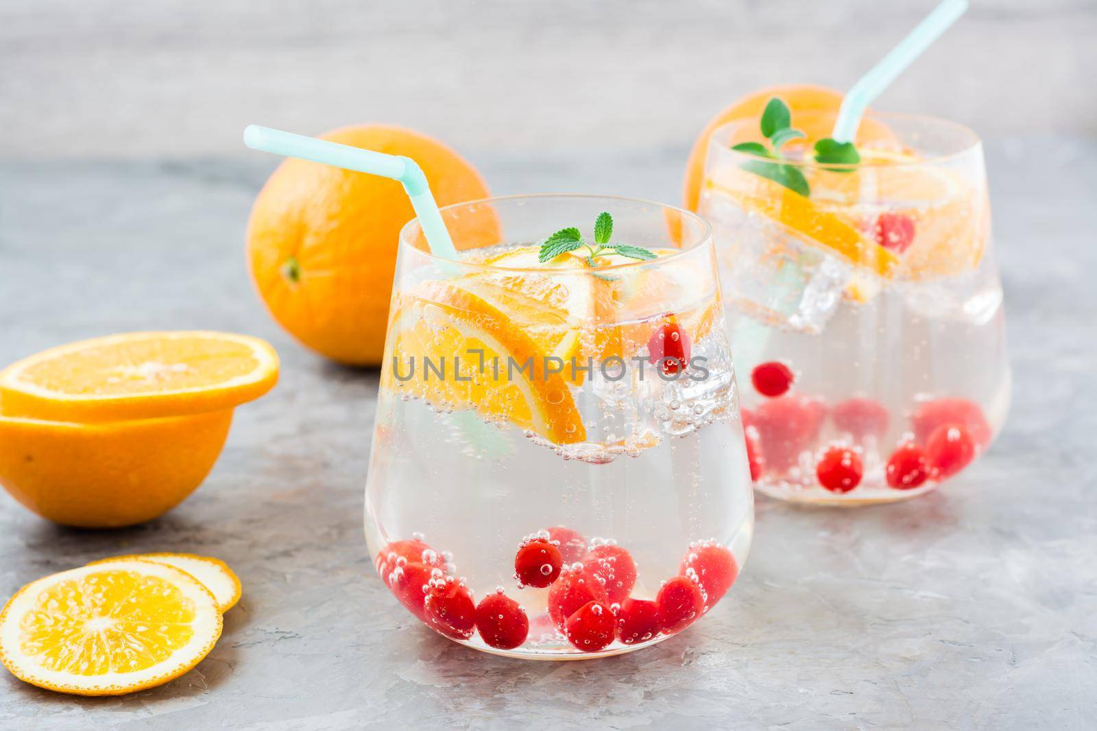 Hard seltzer cocktail with orange, cranberry and mint in glasses and cut oranges on the table. Alcoholic beverage by Aleruana