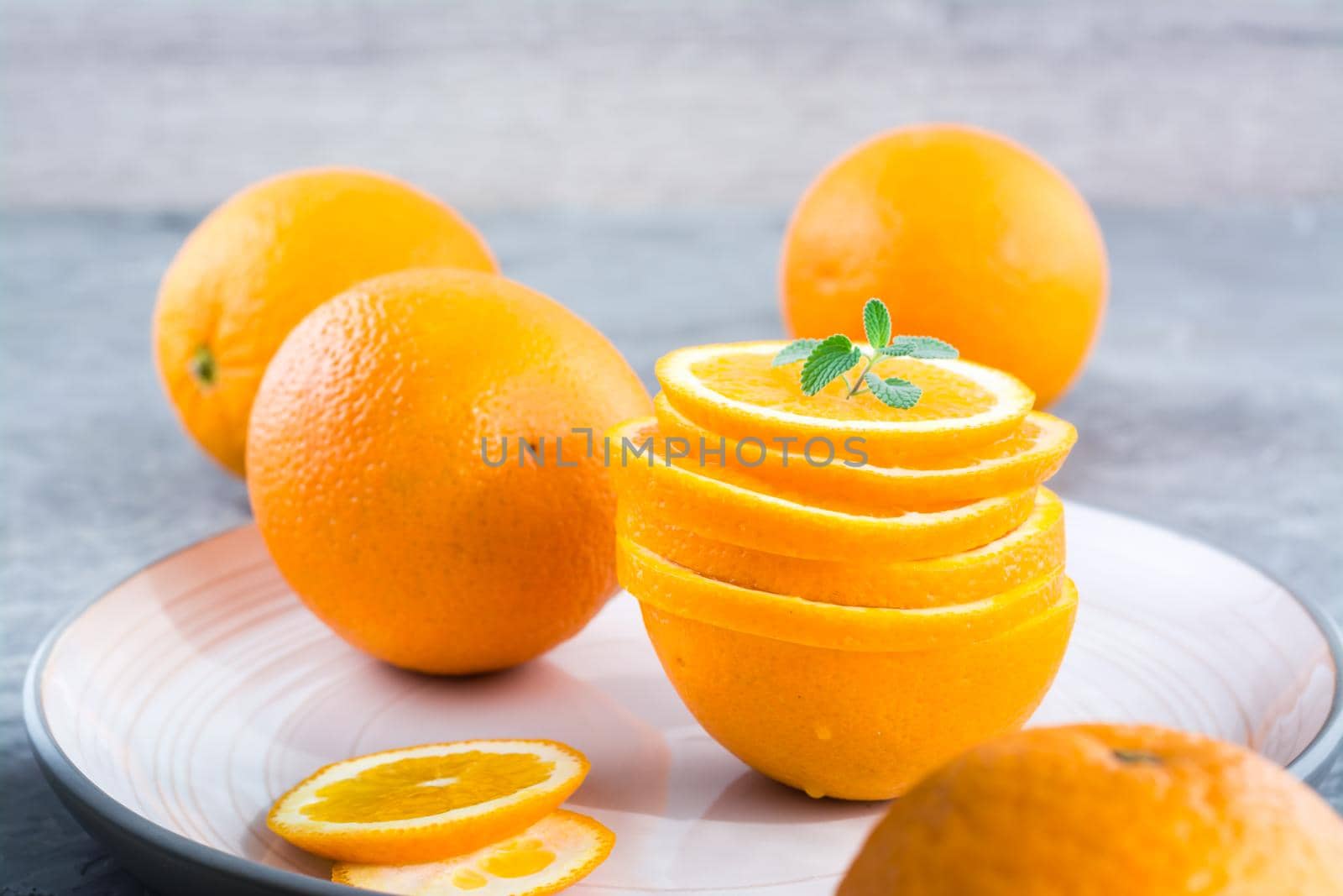 Fresh orange slices in a stack and mint leaves on a plate on the table by Aleruana