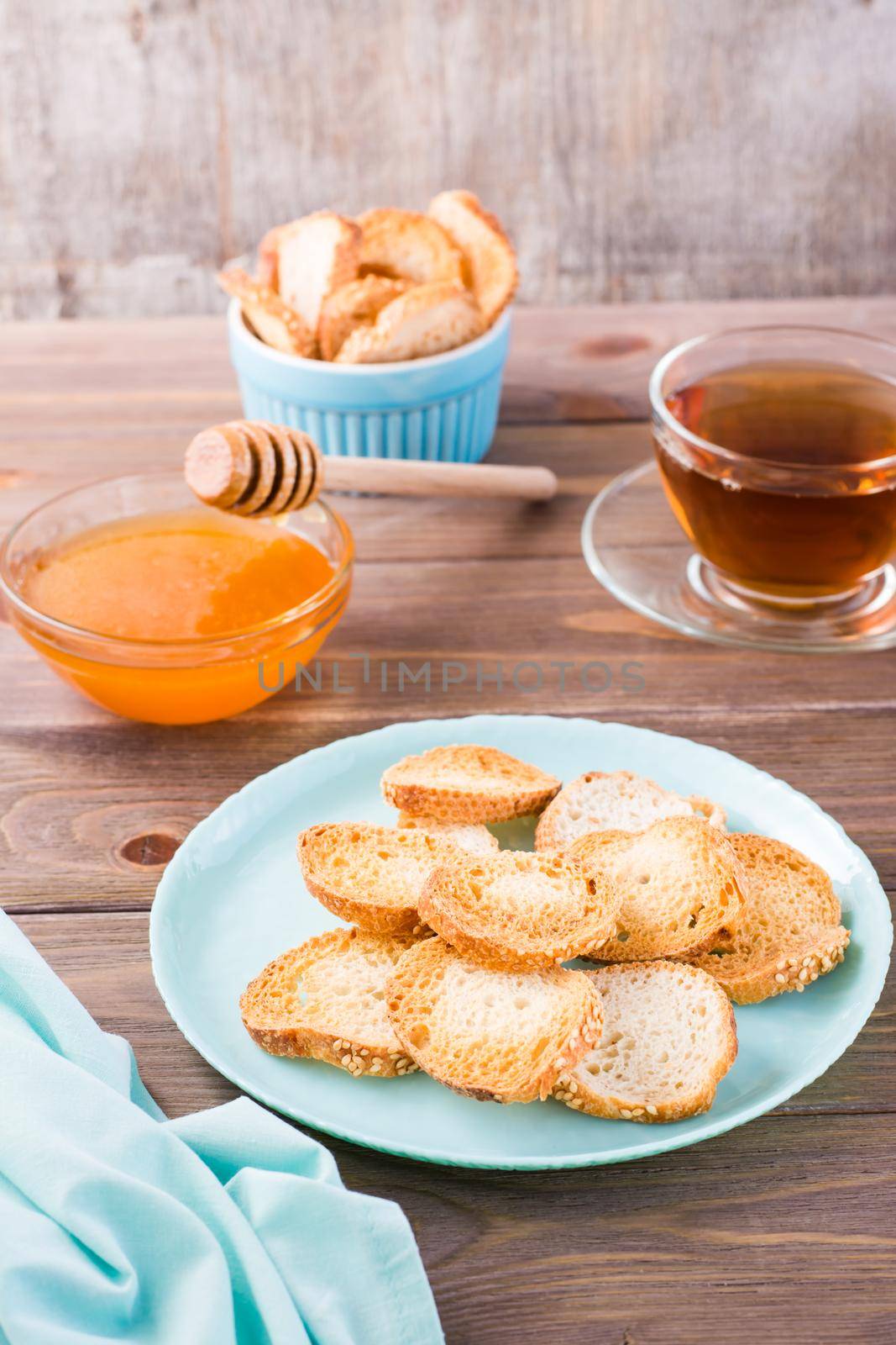 Small baguette toast on a plate on a wooden table. Homemade tea with honey. Vertical view by Aleruana