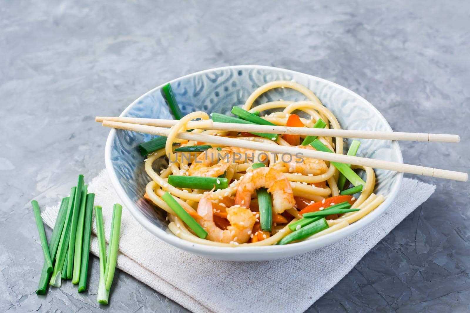 Ready to eat udon and wok noodles with prawns, peppers and onions in a plate and chopsticks on the table. Chinese food by Aleruana