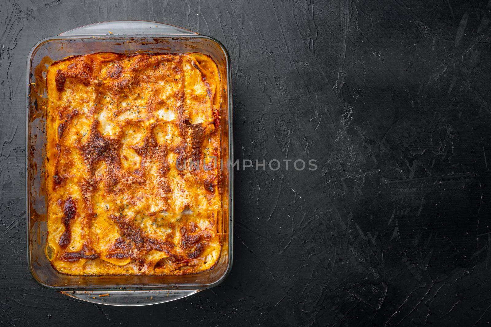 Traditional lasagna made with minced beef bolognese sauce topped with basil leafs set, in baking tray, on black stone background, top view, flat lay, with copy space for text