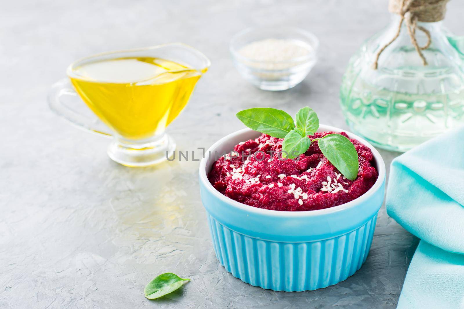 Baked beet hummus in a bowl with sesame seeds and basil on the table. Close-up