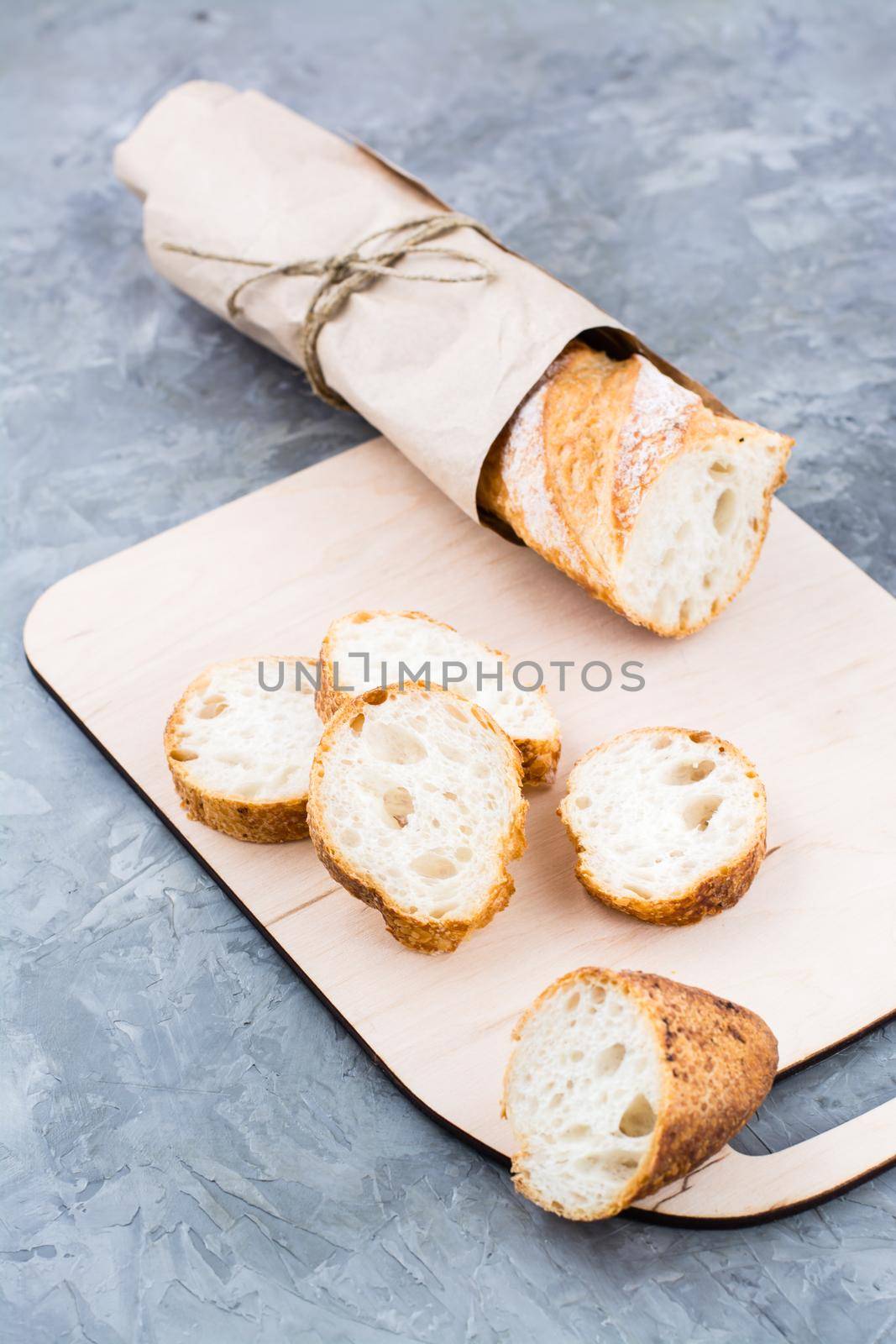 Fresh baguette in wrapping paper cut into pieces on a cutting board on a table. Vertical view by Aleruana