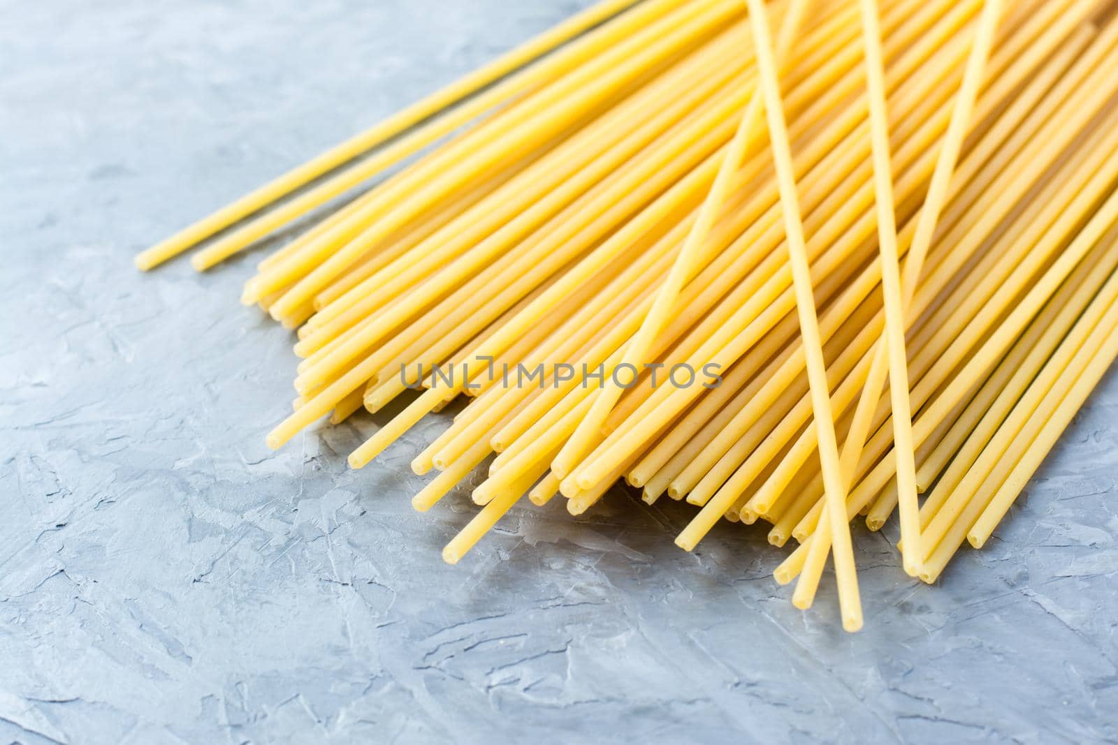 Uncooked long spaghetti on a gray concrete background. Mediterranean food by Aleruana