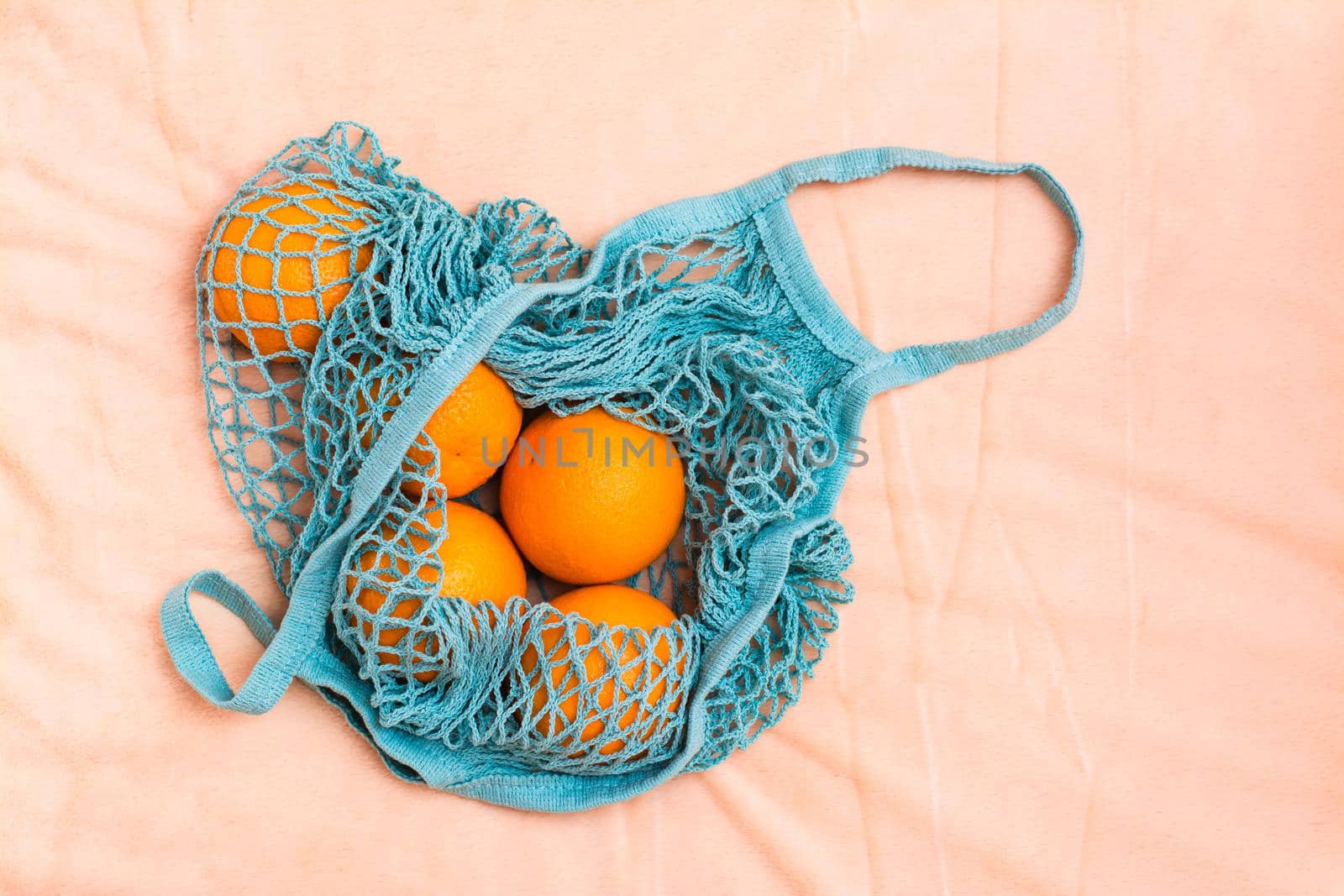 Fresh oranges in a mesh bag on a fabric background. Zero waste