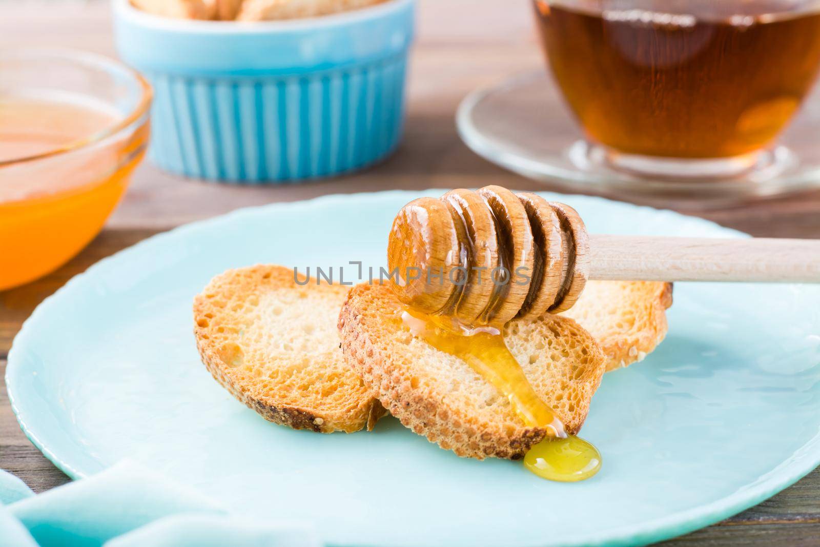 Small baked baguette toast with hot honey on a plate on a wooden table. Homemade tea. Close-up
