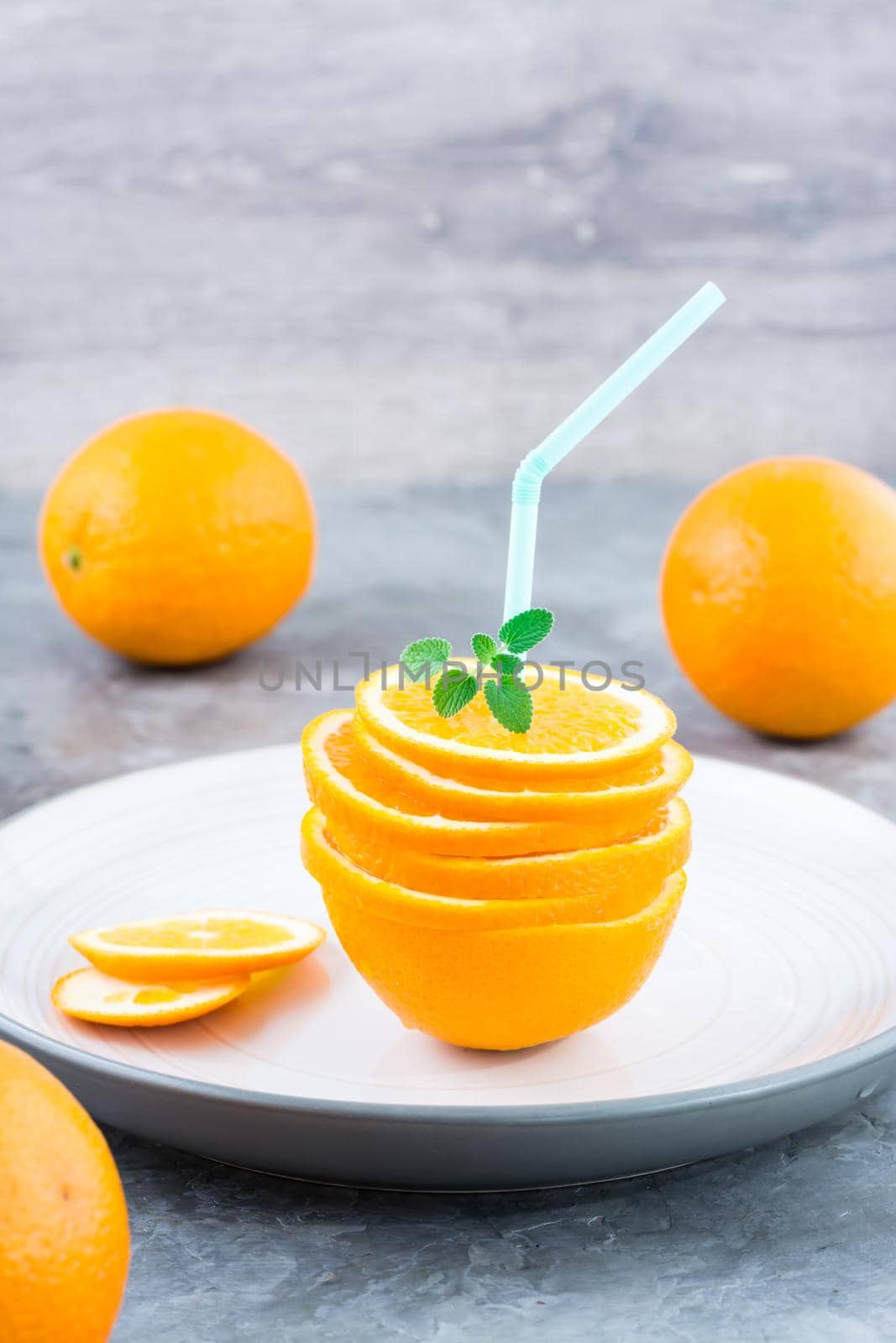 Fresh orange slices in a stack, mint leaves and a straw for a drink. Simulated orange juice. Vertical view by Aleruana