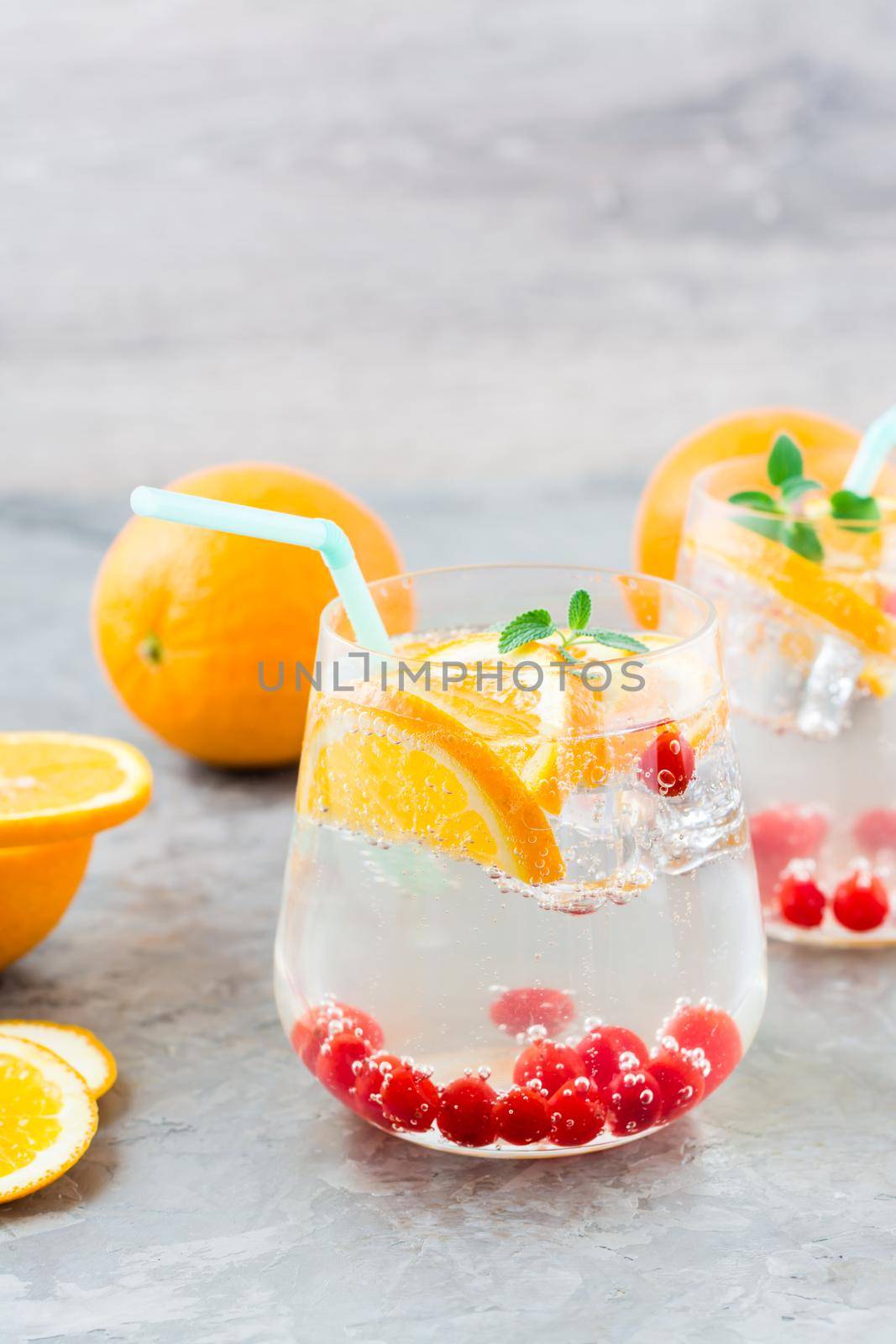 Hard seltzer cocktail with orange, cranberry and mint in glasses on the table. Alcoholic beverage. Vertical view by Aleruana