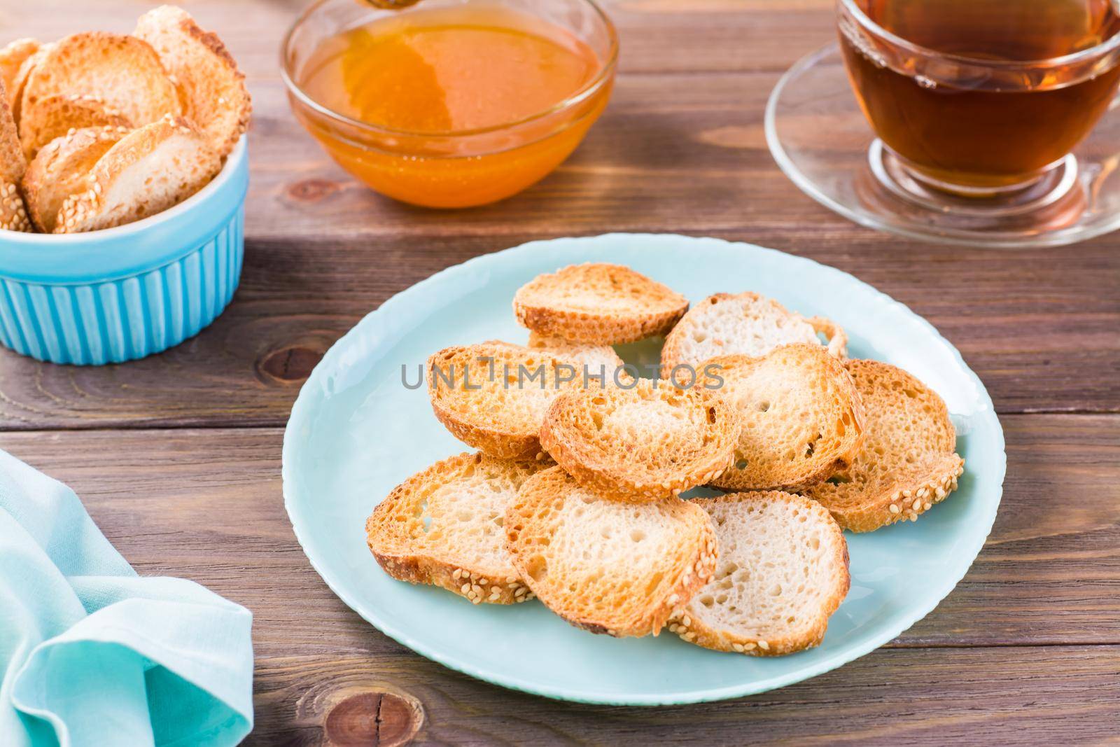 Small baguette toast on a plate on a wooden table. Homemade tea with honey by Aleruana