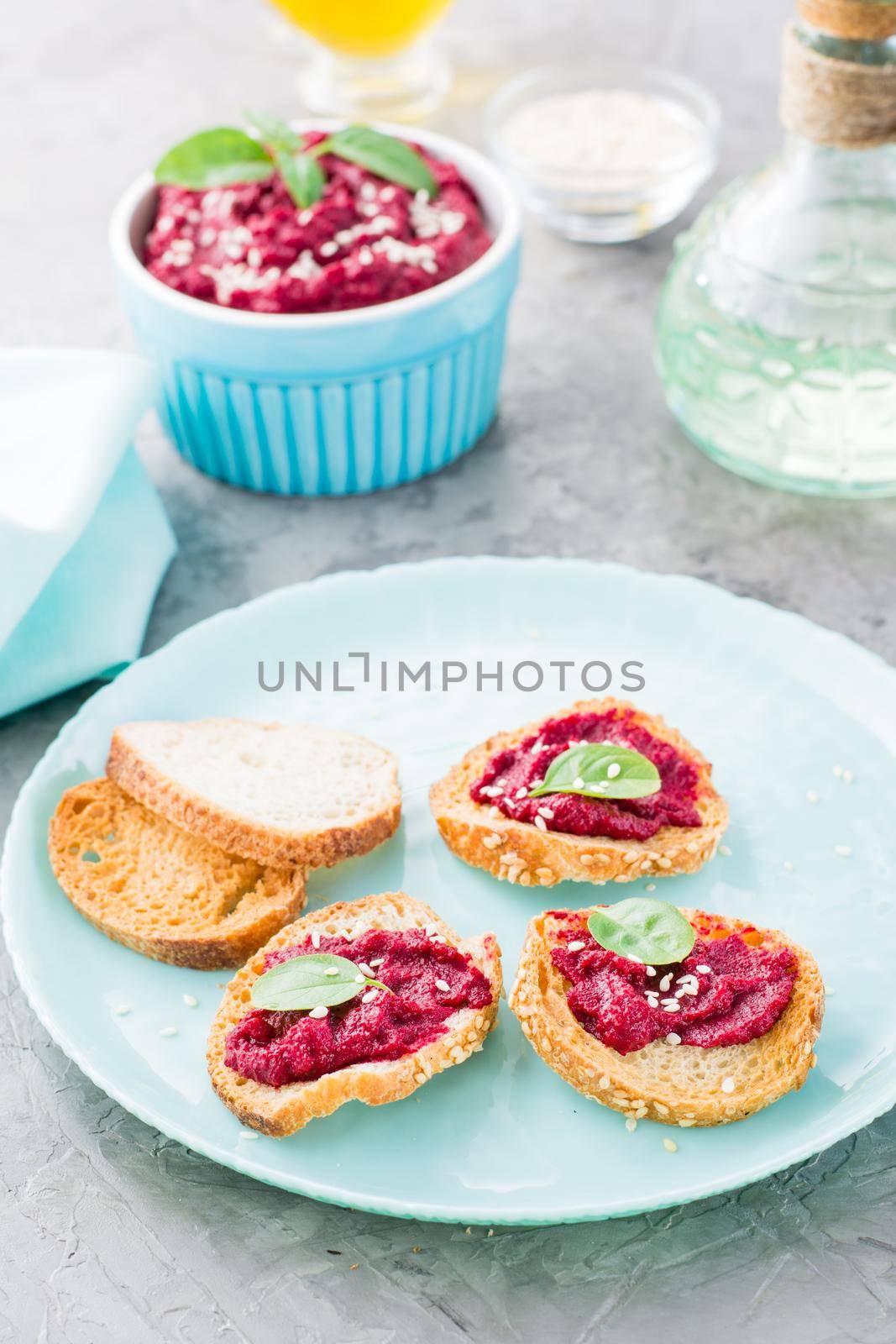 Homemade bruschetta with beetroot hummus on small baked baguette toast on a plate and a bowl of hummus on the table. Vertical view by Aleruana