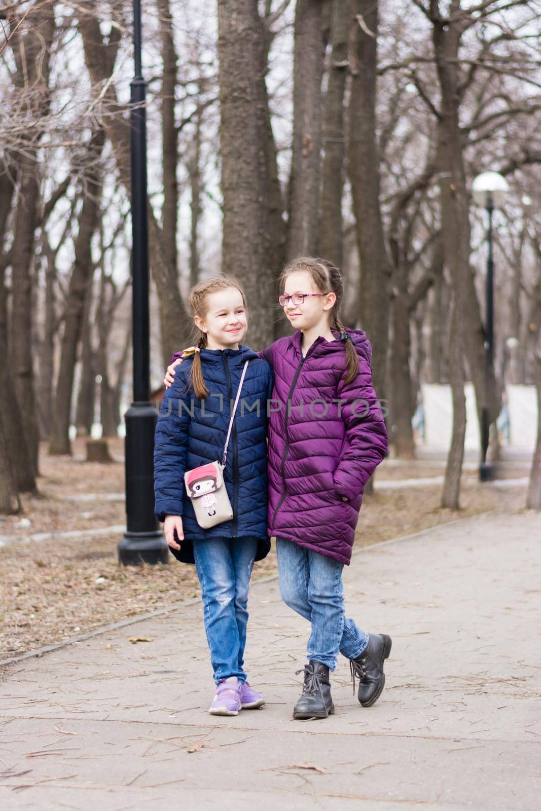 Two girls sisters walk along the path in the city park in early spring and smile by Aleruana