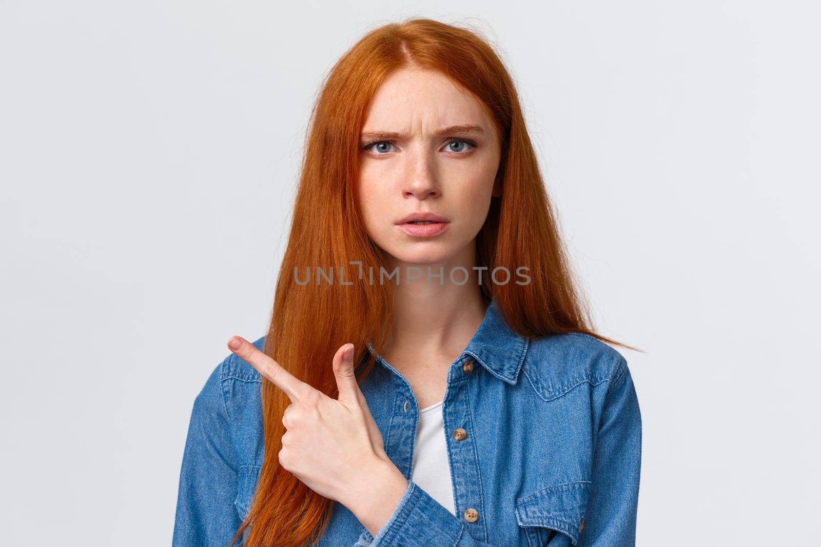Close-up portrait serious-looking skeptical and displeased angry bothered redhead girlfriend waiting explanation, demand answers as seing something unplesant, pointing finger left.