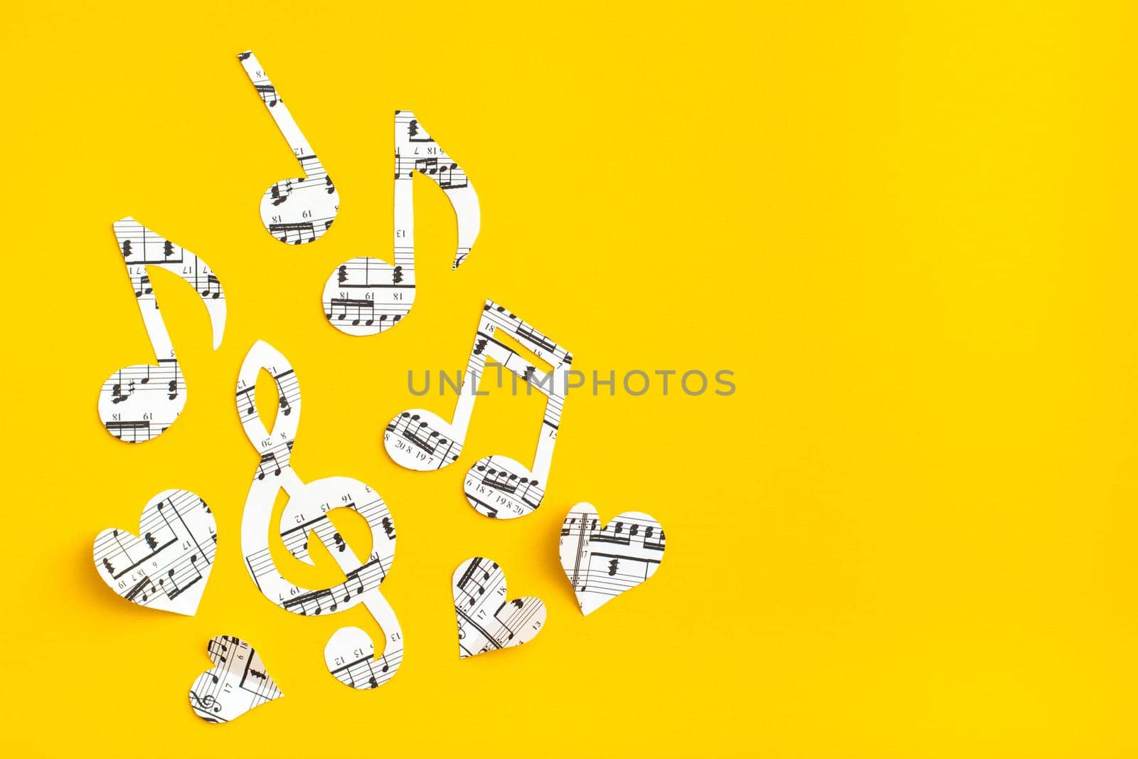 Musical notes, clef and hearts cut from paper with musical text on yellow background. Copy space