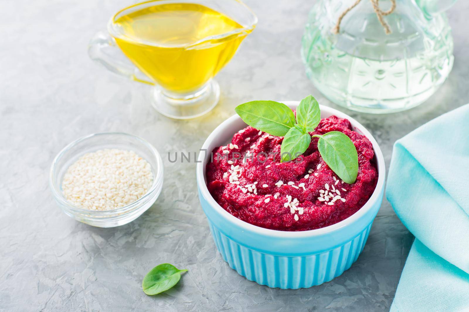 Baked beet hummus in a bowl with sesame seeds and basil on the table