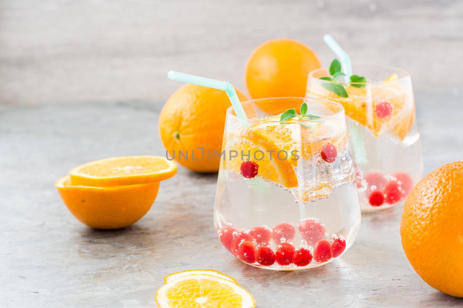 Hard seltzer cocktail with orange, cranberry and mint in glasses and cut oranges on the table. Alcoholic highly carbonated drink
