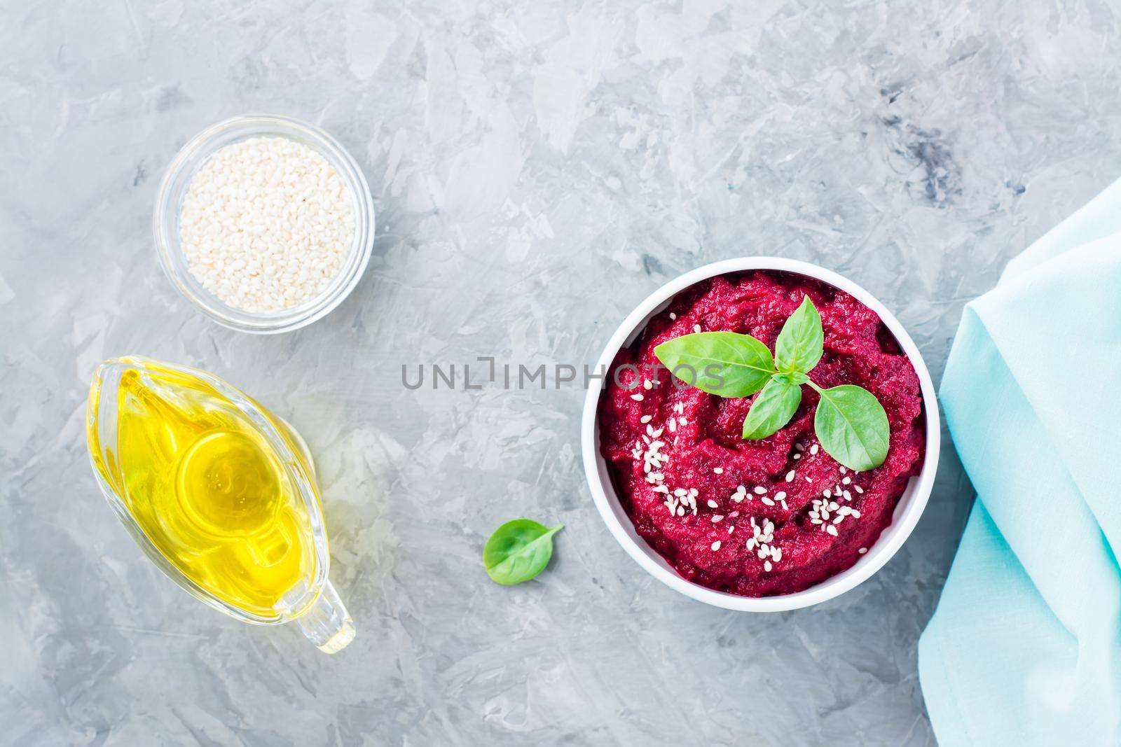 Homemade baked beetroot hummus in a bowl with sesame seeds and basil on the table. Top view