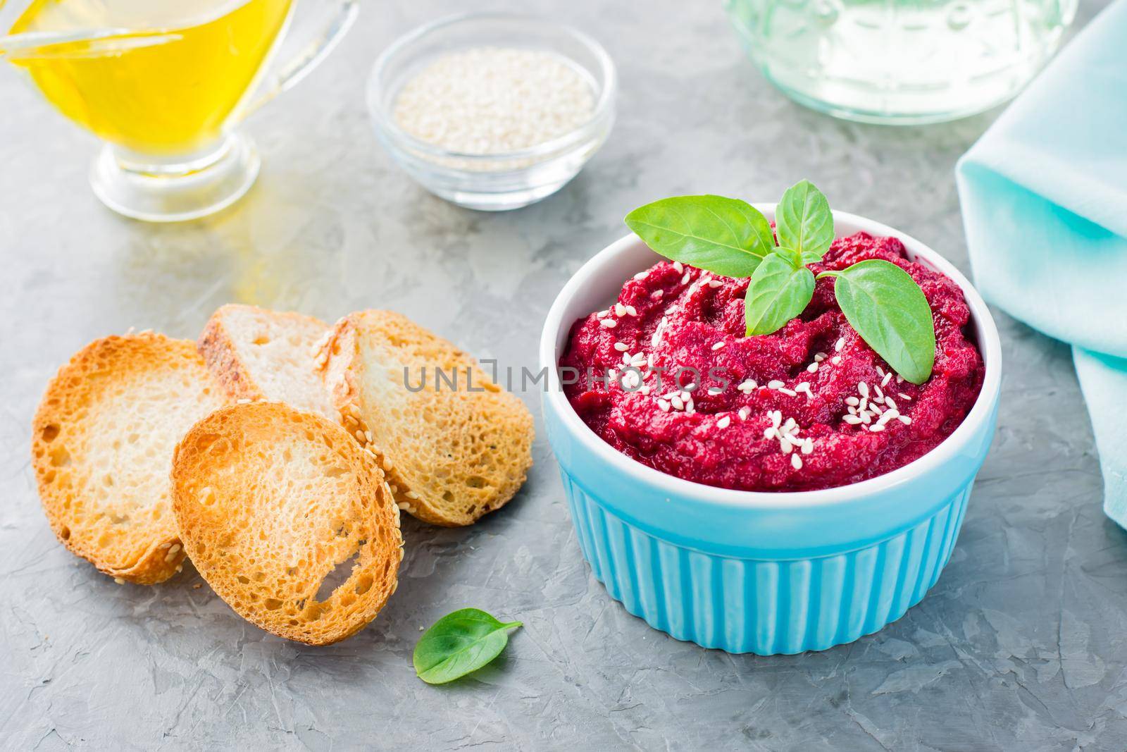 Homemade baked beet hummus in a bowl with sesame seeds and basil and baked small toast on the table