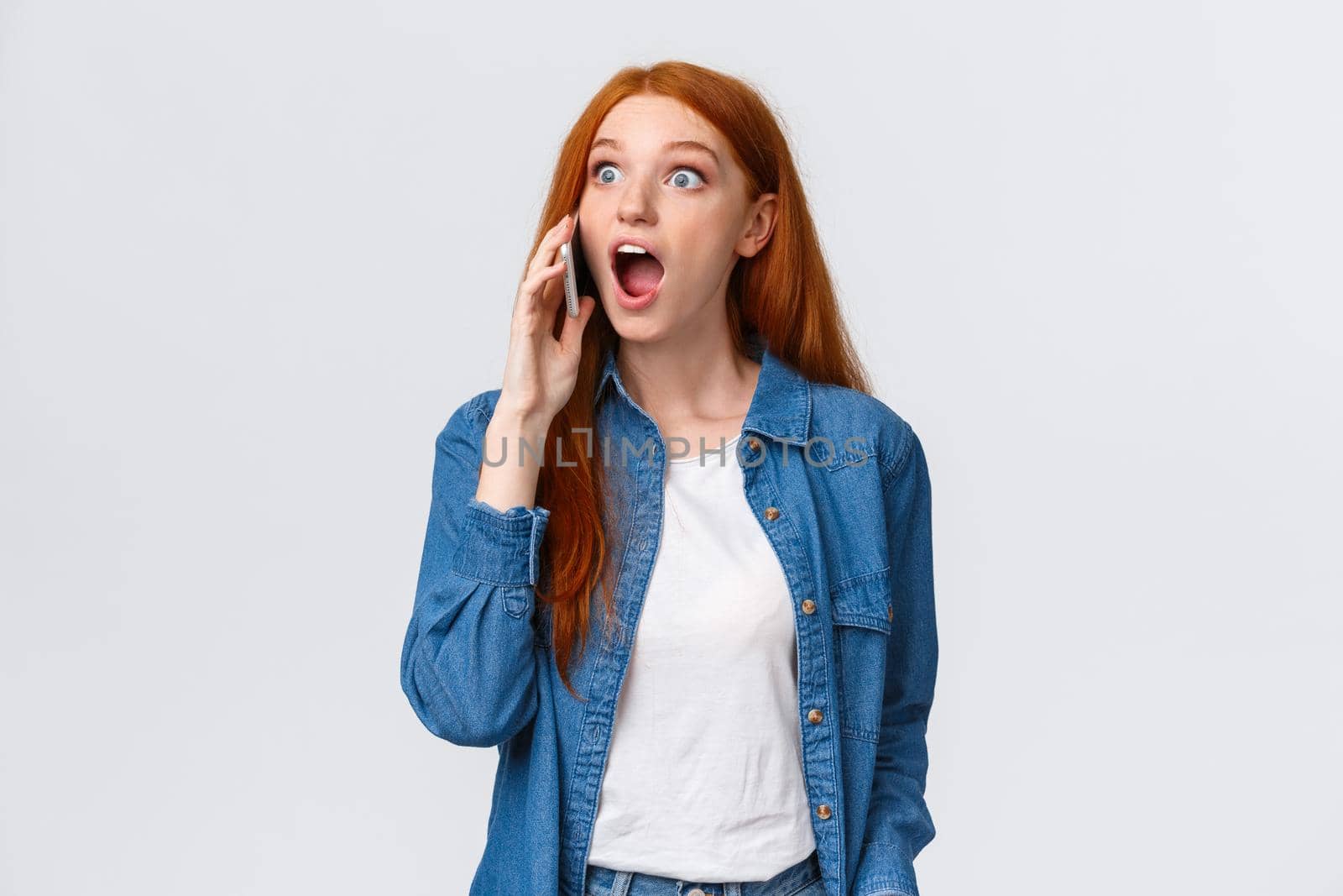 Girl hears amazing great news on phone. Excited lucky redhead girl pick-up phone realises she won challenge, gasping amazed and astonished, holding smartphone near ear, popping eyes surprised.