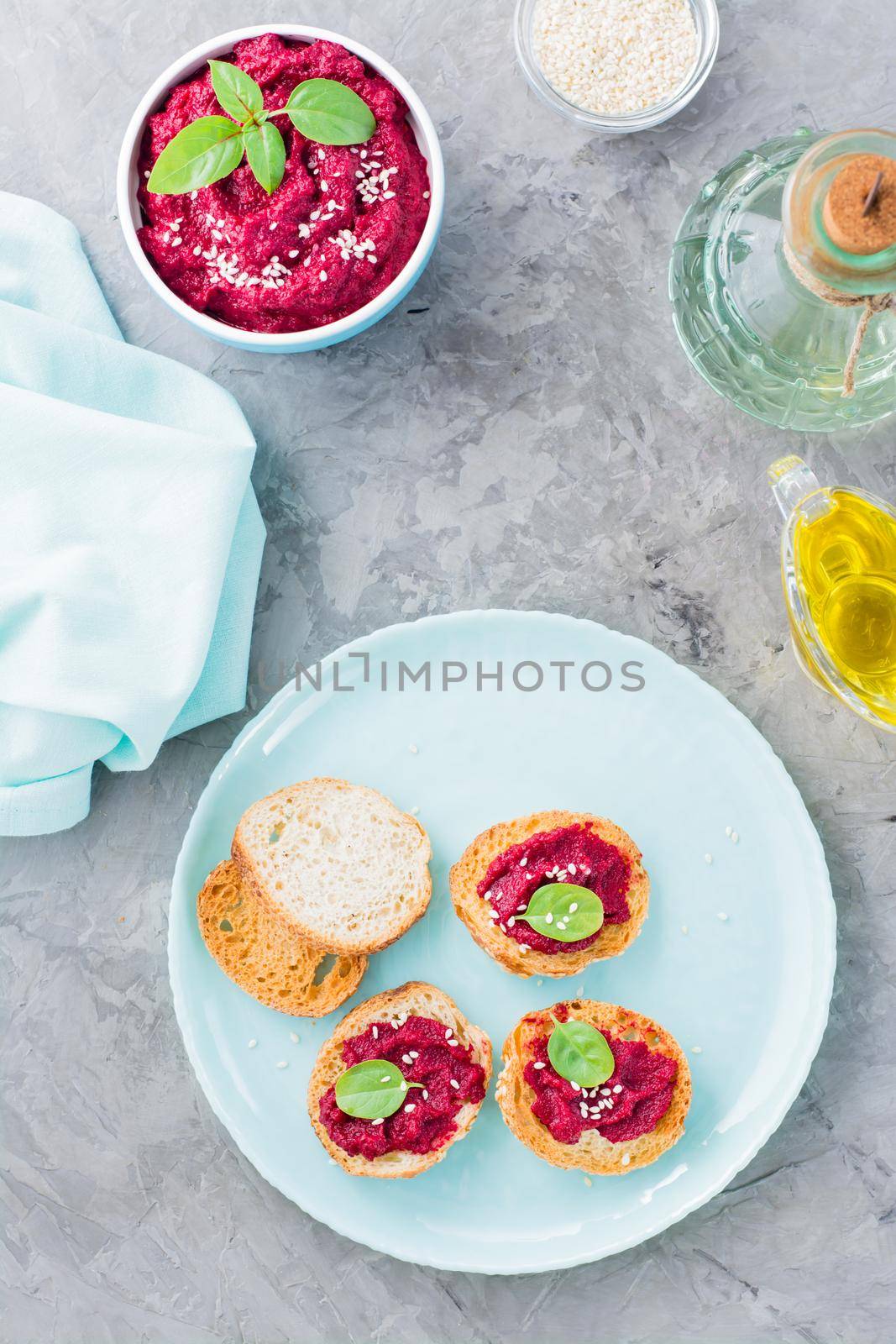 Homemade bruschetta with beetroot hummus on small baked baguette toast on a plate and a bowl of hummus on the table. Vertical and top view