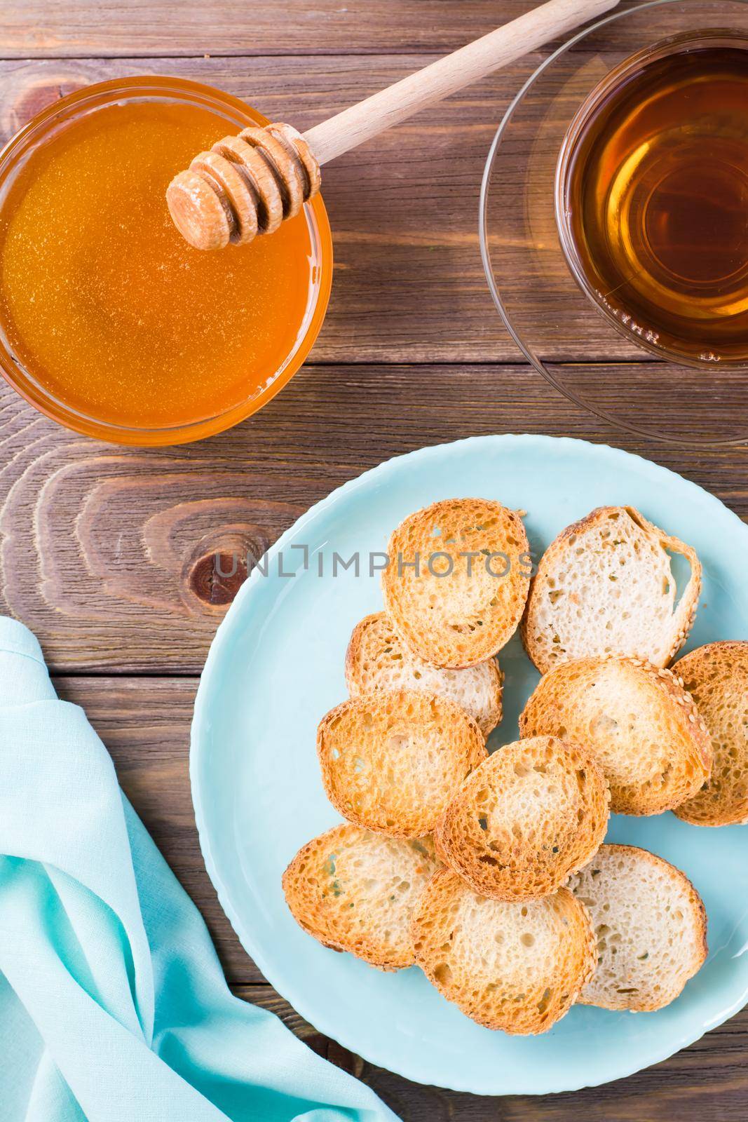 Small baguette toast on a plate on a wooden table. Homemade tea with honey. Top and vertical view by Aleruana