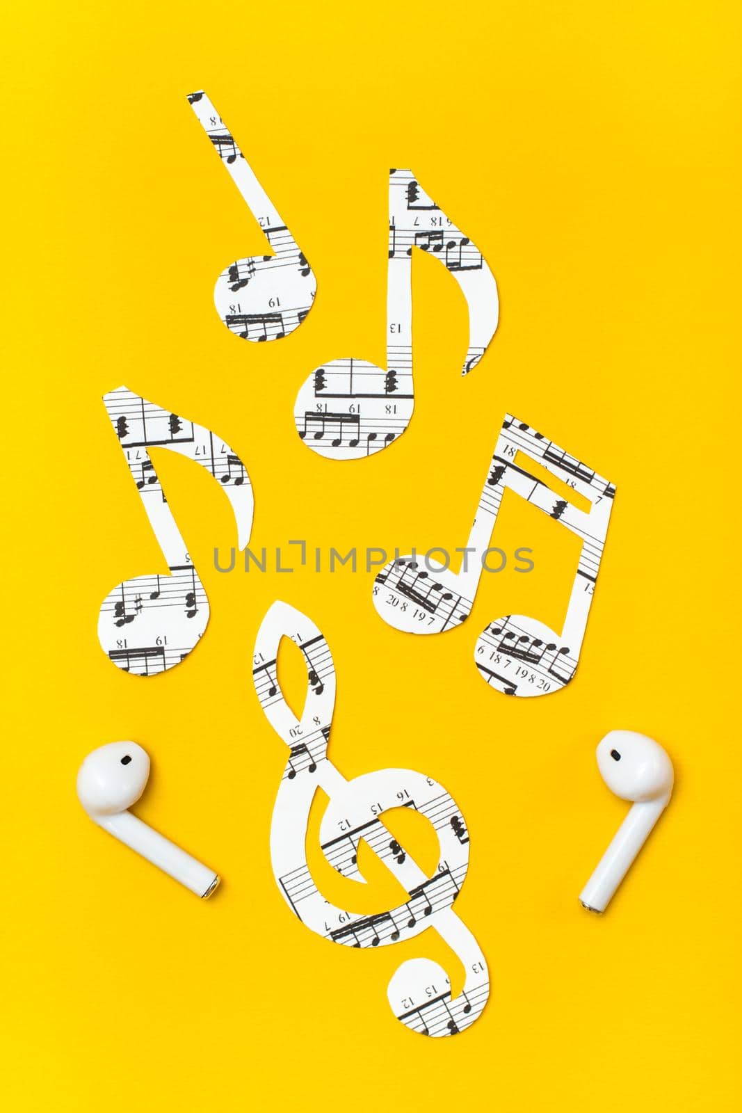 Wireless headphones and music notes cut from paper on a yellow background. Music imitation concept. Vertical view by Aleruana