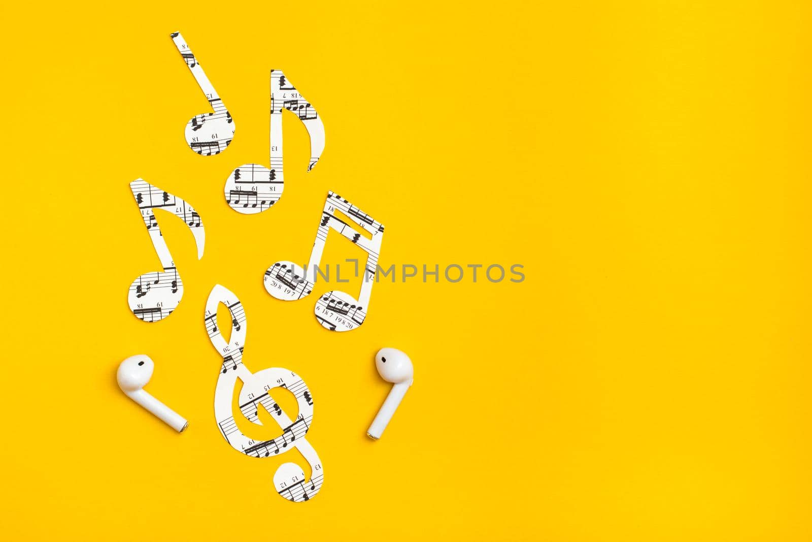 Wireless headphones and music notes cut from paper on a yellow background. Music imitation concept. Copy space by Aleruana