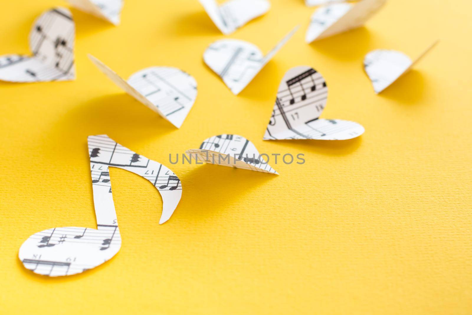 Musical notes, clef and hearts cut from paper with musical text on yellow background by Aleruana