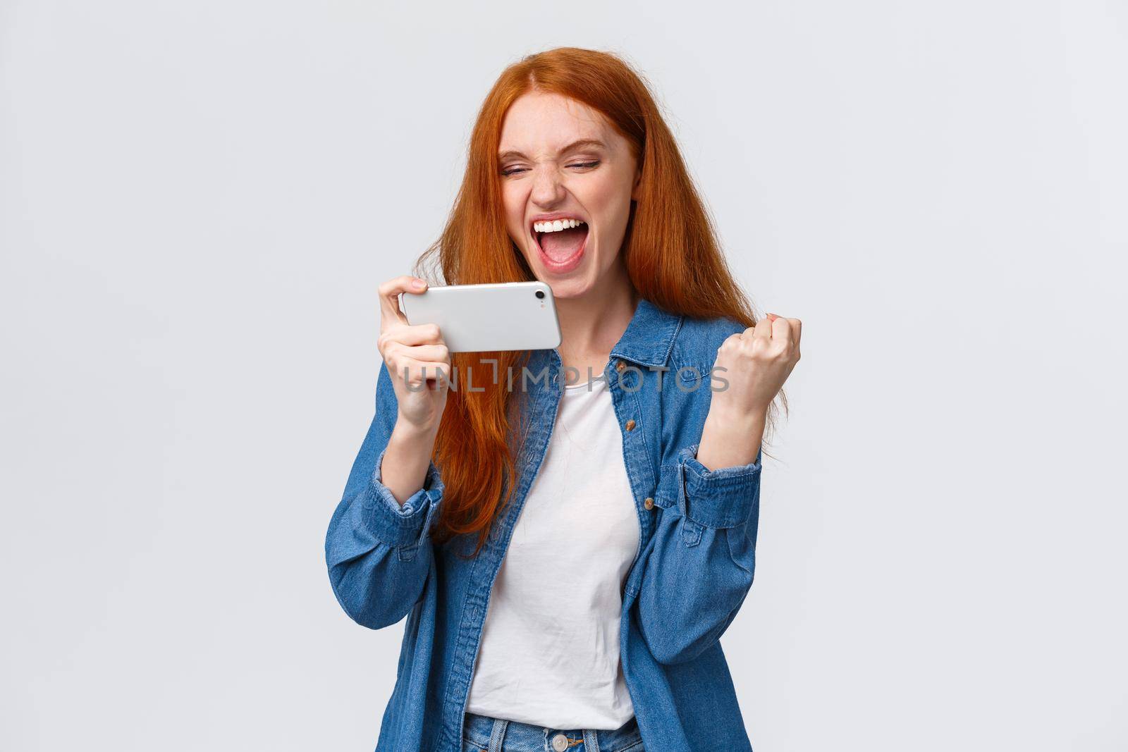 Confident and sassy good-looking redhead woman beat score, watching tennis match online on smartphone and cheering for player, fist pump delighted, celebrating success, winning in mobile game.