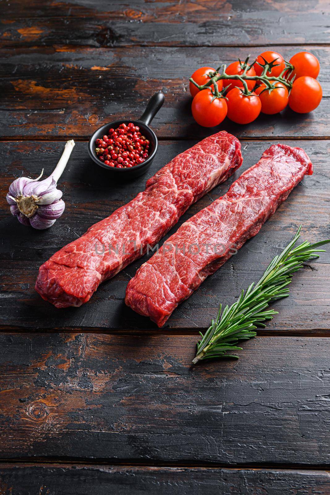 Denver steak two fresh, raw steaks from the cut of beef or organic top blade with herbs on old dark wooden table surface side view space for text vertical by Ilianesolenyi