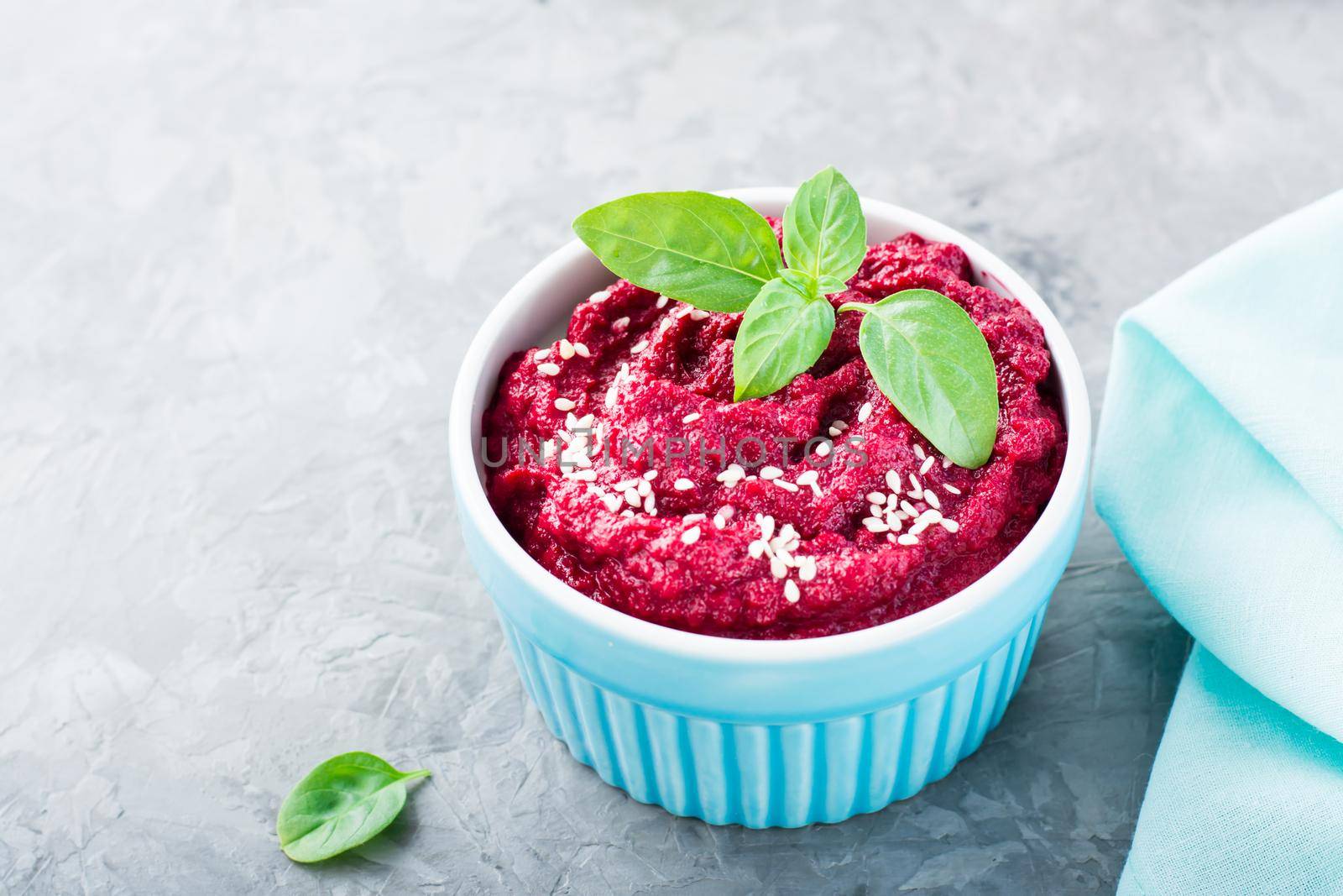 Homemade baked beetroot hummus in a bowl with sesame seeds and basil on the table. Close-up