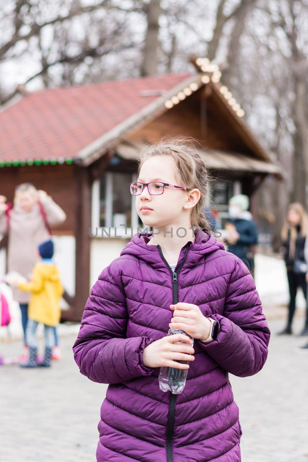 A cute girl in glasses holds a bottle with water bought in a food truck in a city park. Takeaway food by Aleruana