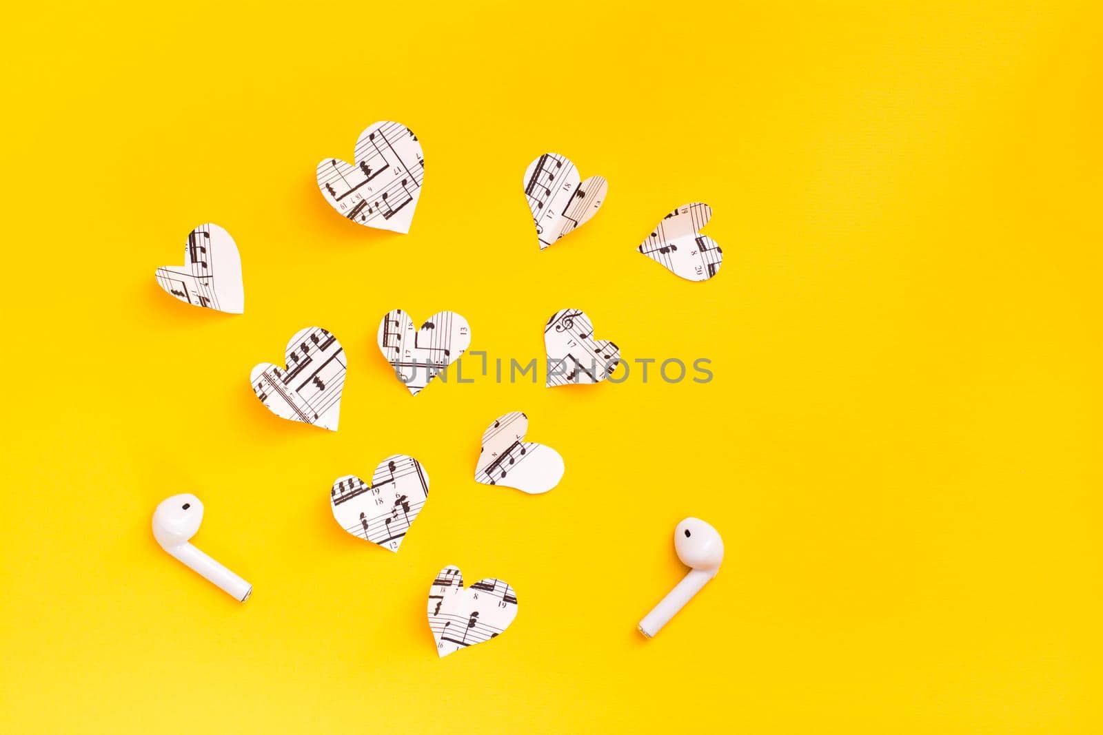 Wireless headphones and hearts cut from the music text on a yellow background. Love for music through gadgets. Copy space