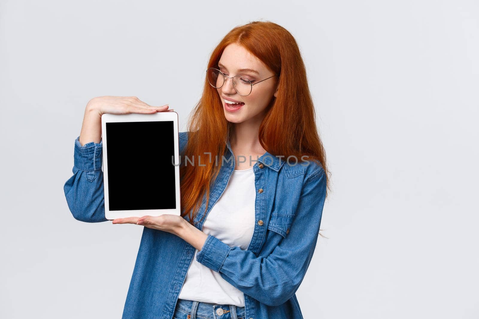 Technology and people concept. Attractive creative young redhead girl creating design project for university, holding digital tablet and introduce something on device screen, white background.