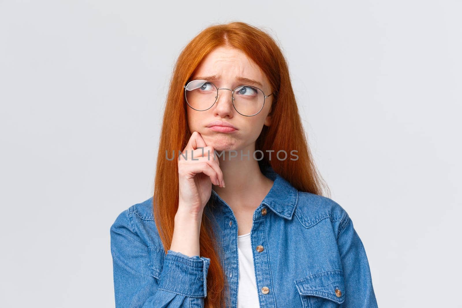 Uneasy sulky cute timid redhead college girl in glasses, look up thoughtful and dreamy, pouting unhappy feeling sad, regret comming party, standing white background indecisive and upset.